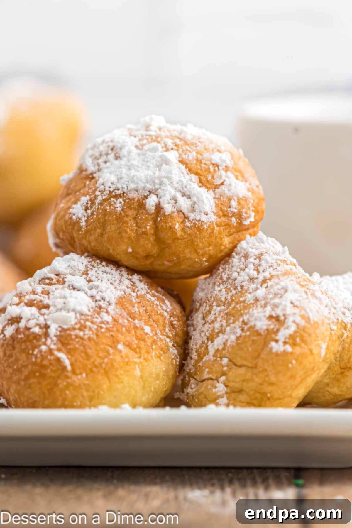 A close-up shot of a plate piled high with golden, freshly fried funnel cake bites, generously coated in powdered sugar, highlighting their inviting texture.