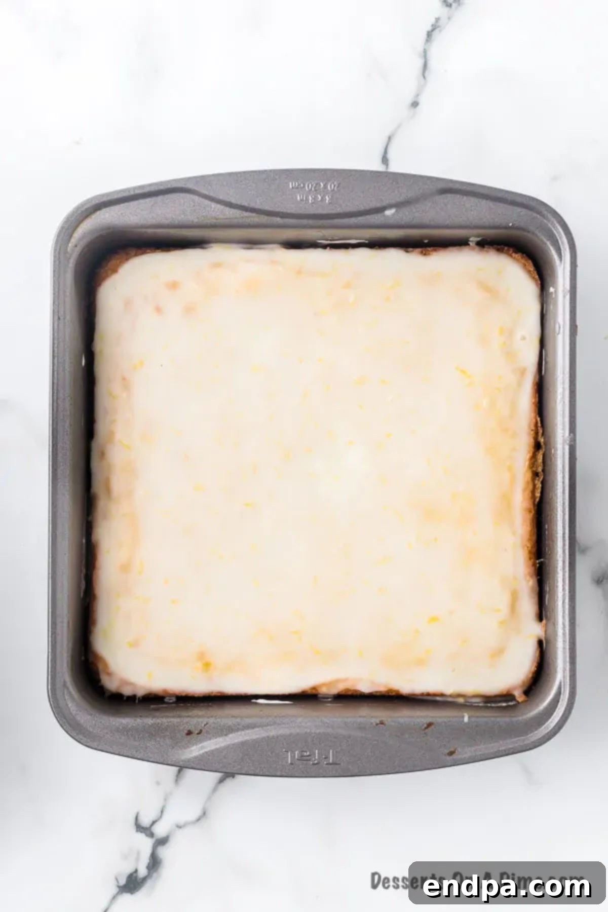 Baked lemon brownies in a pan with the lemon glaze poured over the top.