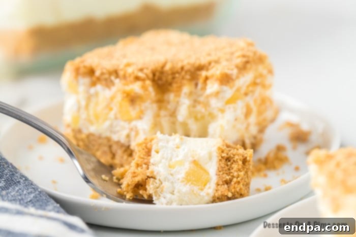 A square slice of Pineapple Dream Dessert with a bite taken out of it, showing layers of golden crust, creamy white filling, and a pineapple-studded top.