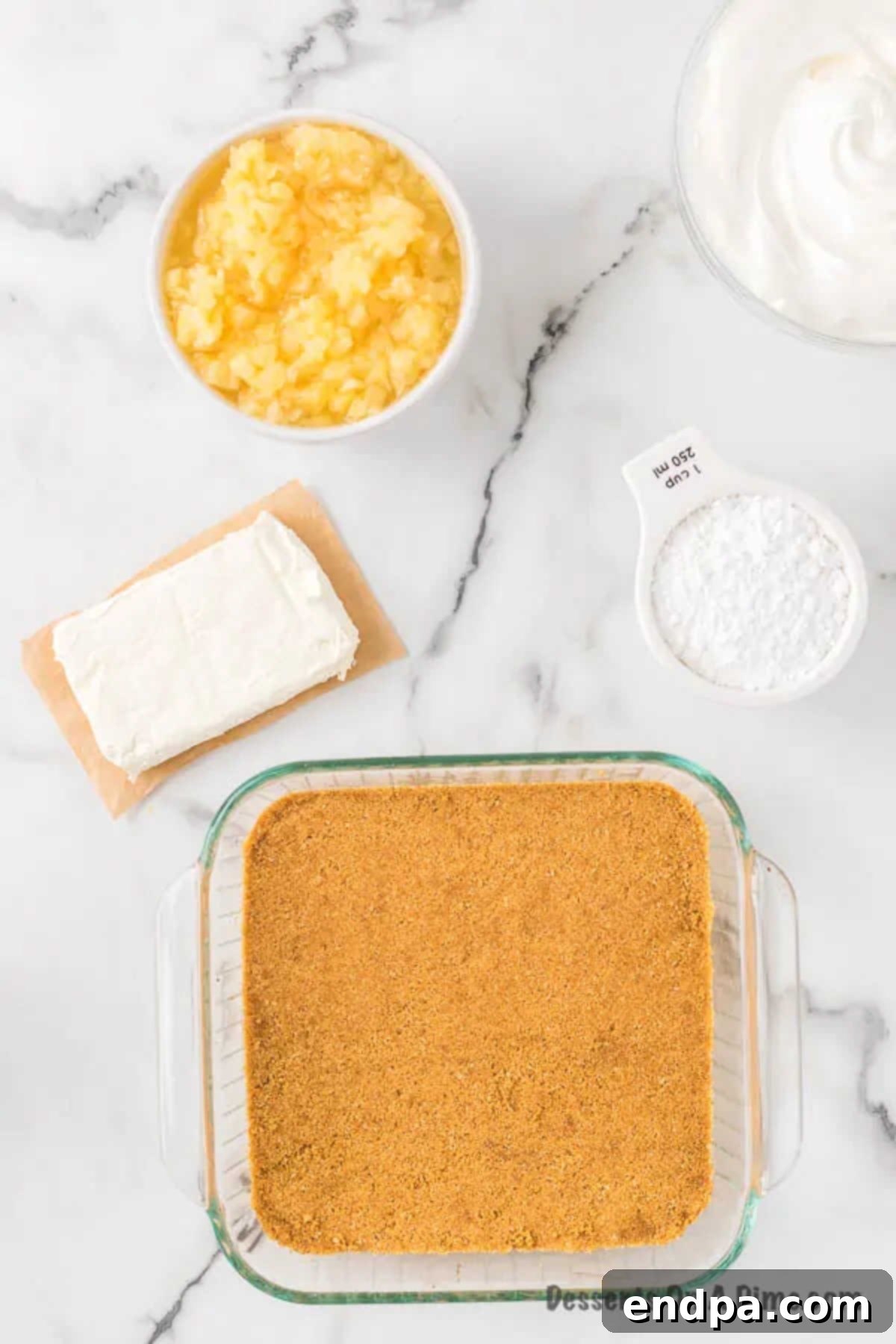 Graham cracker crumbs pressed firmly into the bottom of a 9x9 baking dish, ready for baking.