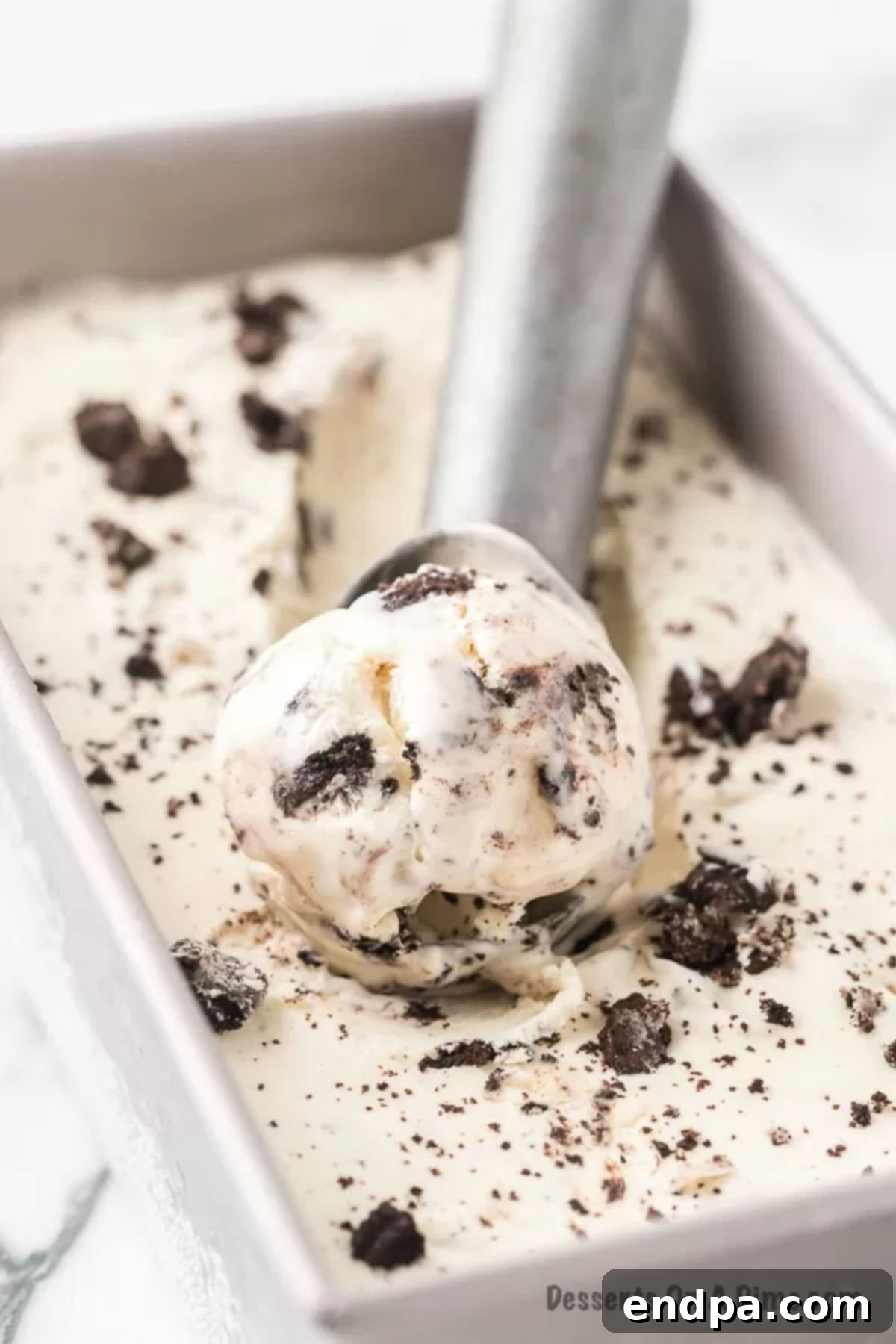 Midnight Cookie Swirl Ice Cream 2 Cookies and Cream Ice Cream being scooped out of loaf pan, showing its rich texture and chunks of Oreo cookies.