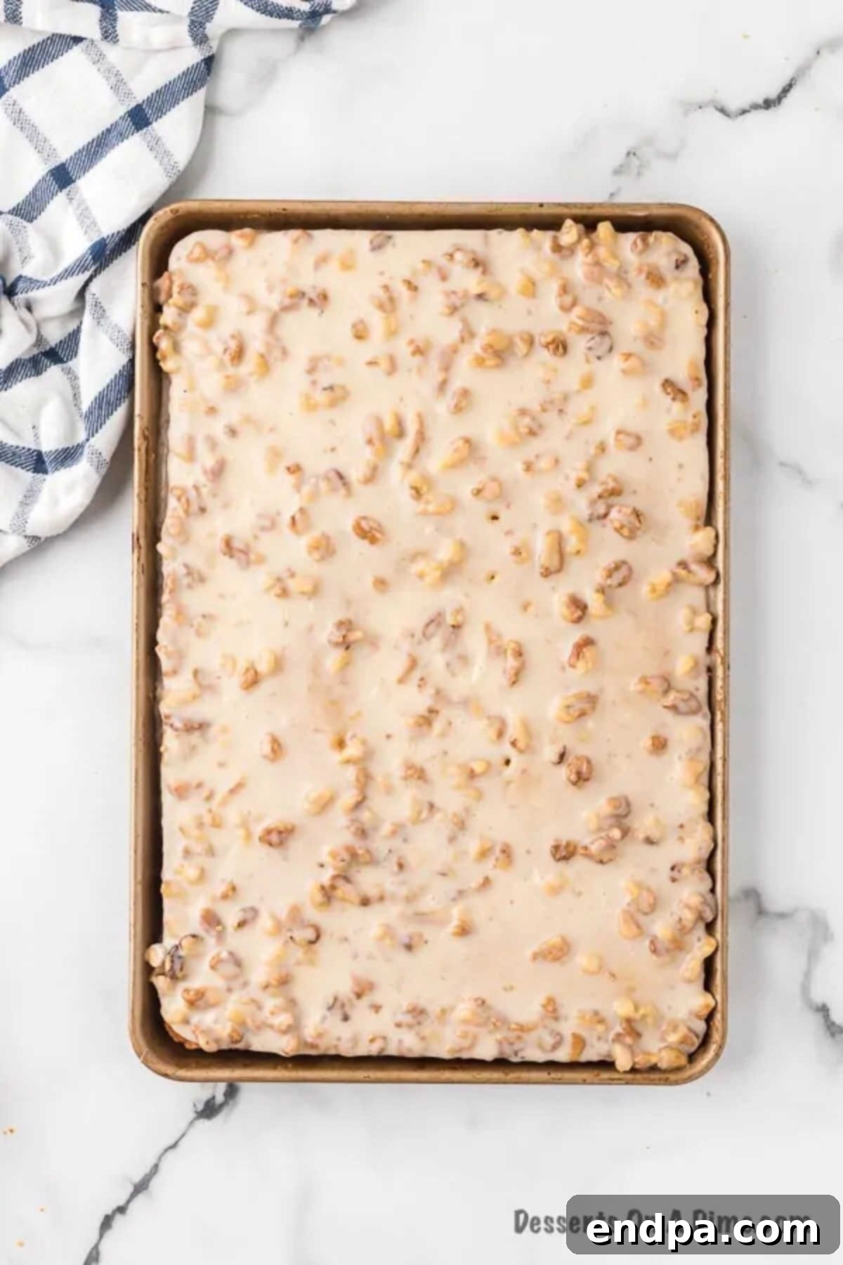 Warm, glistening white icing being spread generously over the freshly baked sheet cake.