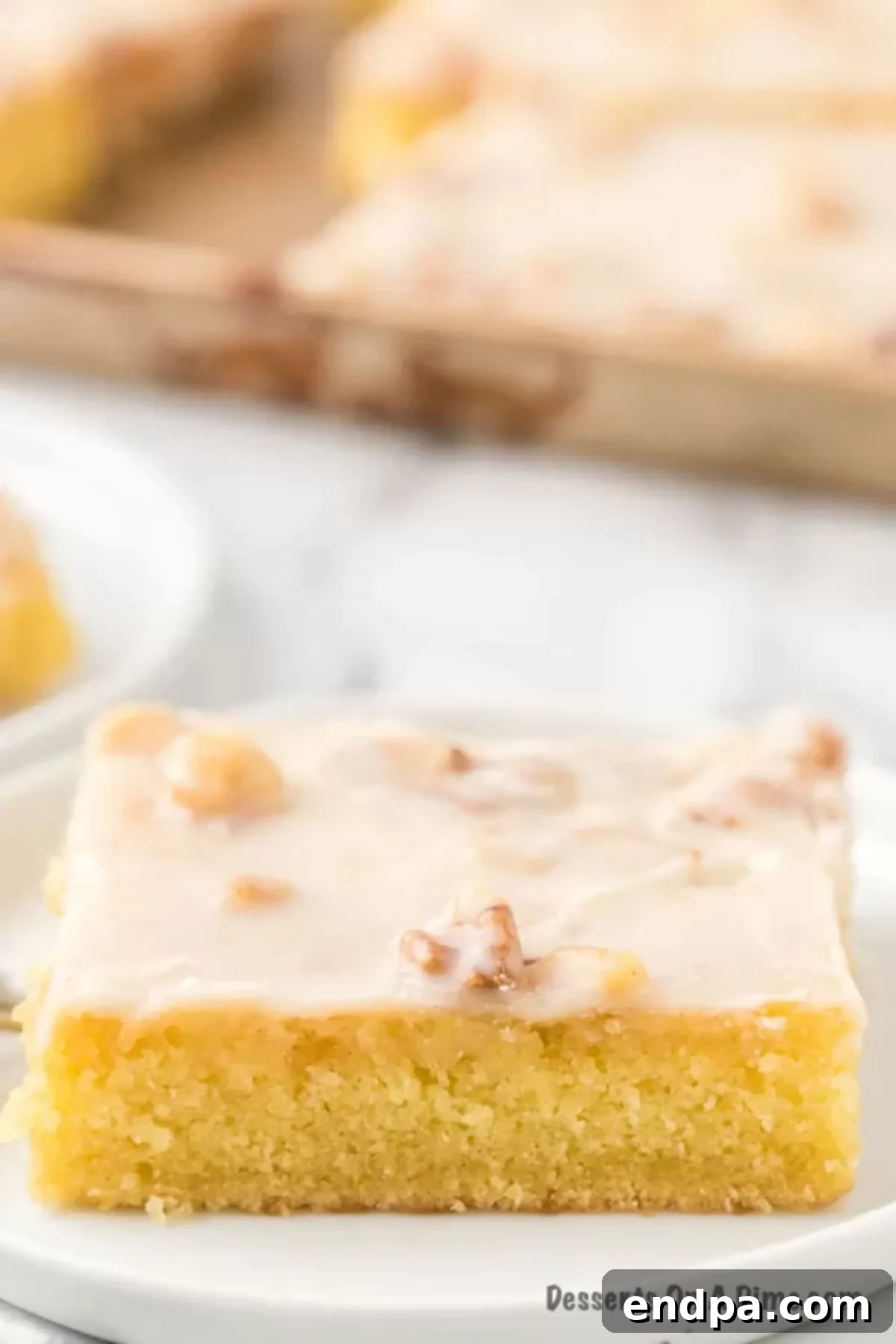 A pristine slice of White Texas Sheet Cake, rich with frosting and a hint of nuts, on a white plate.