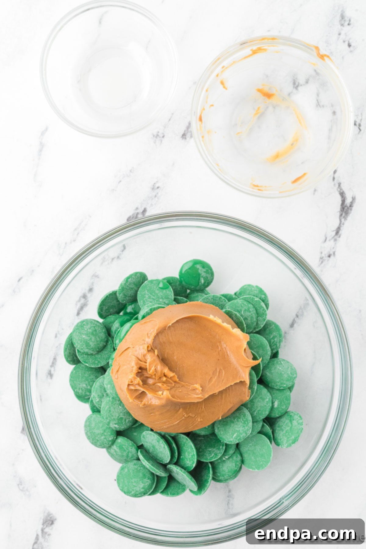 Mixing bowl with green candy melts, peanut butter, and vegetable oil combined and ready for melting.