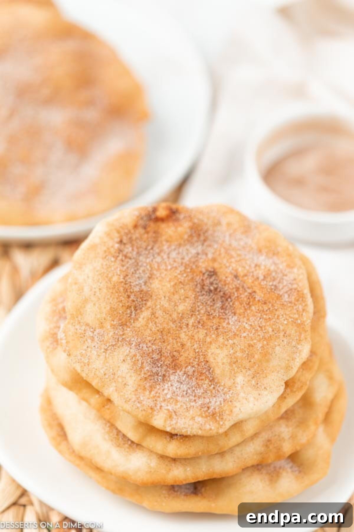 Golden Crispy Elephant Ears Delight 14 Four beautifully fried elephant ears, generously coated with cinnamon sugar, are stacked neatly on a white ceramic plate, ready to be served.