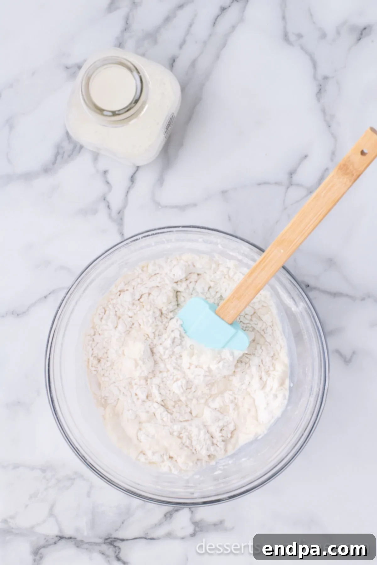 Golden Crispy Elephant Ears Delight 5 Whole milk is being gradually poured into the mixing bowl containing dry ingredients, as a spatula begins to stir the mixture, forming a dough.