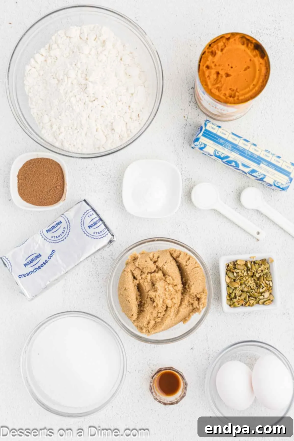 Starbucks-Style Pumpkin Spice Cream Cheese Muffins 3 Ingredients for Pumpkin Muffins - all-purpose flour, pumpkin pie spice, baking soda, brown sugar, eggs, pumpkin puree, softened butter, cream cheese, vanilla extract, and pumpkin seeds laid out on a white surface.