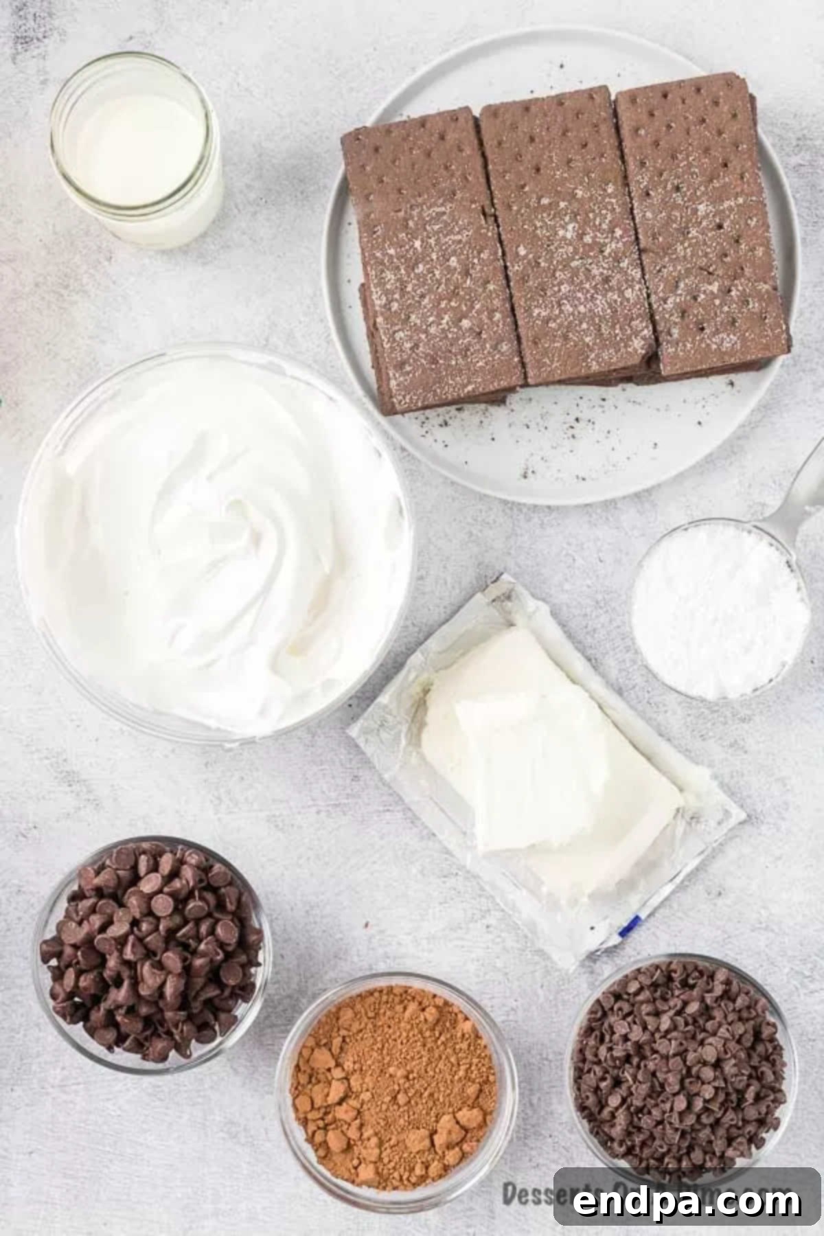 Ingredients for Chocolate Ice Box Cake - chocolate graham crackers, cream cheese, powdered sugar, cool whip, heavy cream, chocolate chips arranged on a wooden surface.
