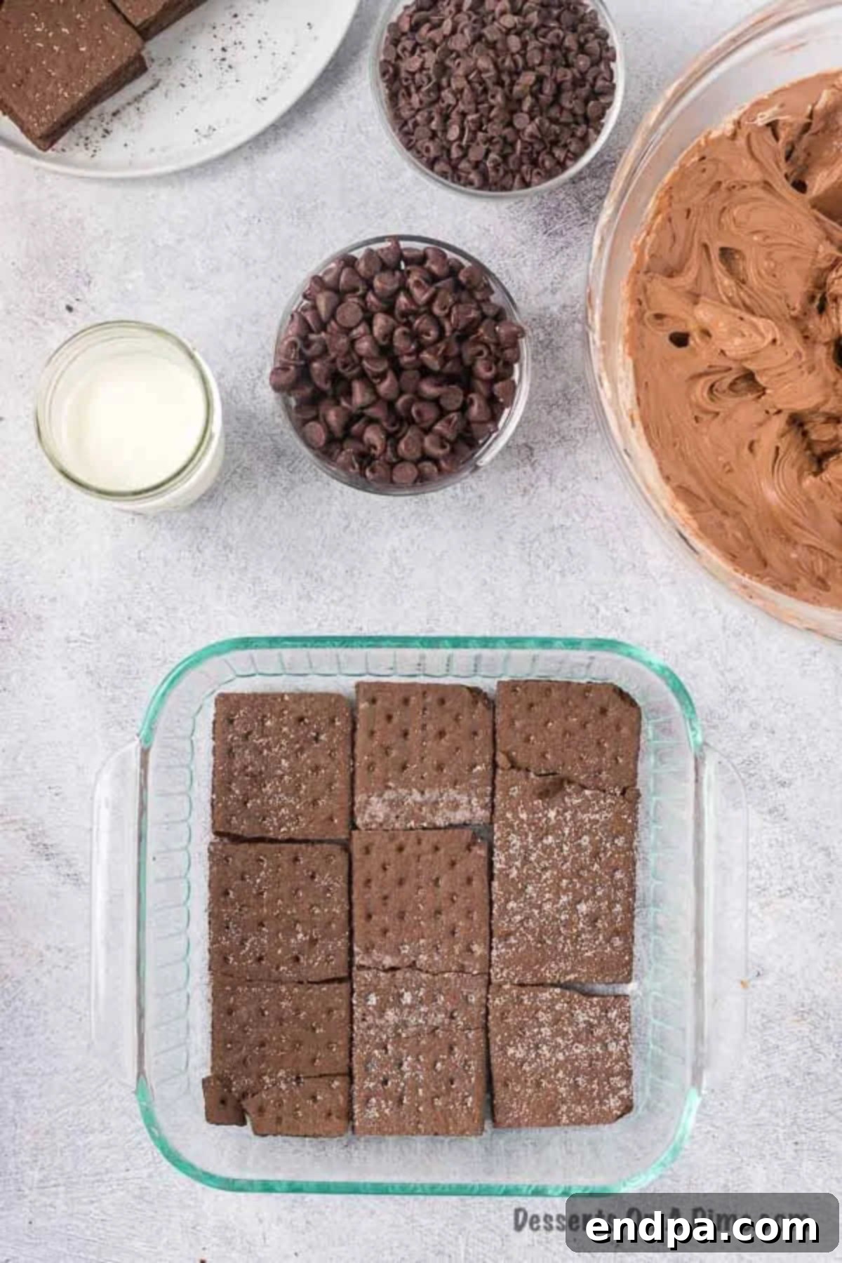 Chocolate graham crackers arranged in a single layer at the bottom of a square baking dish.