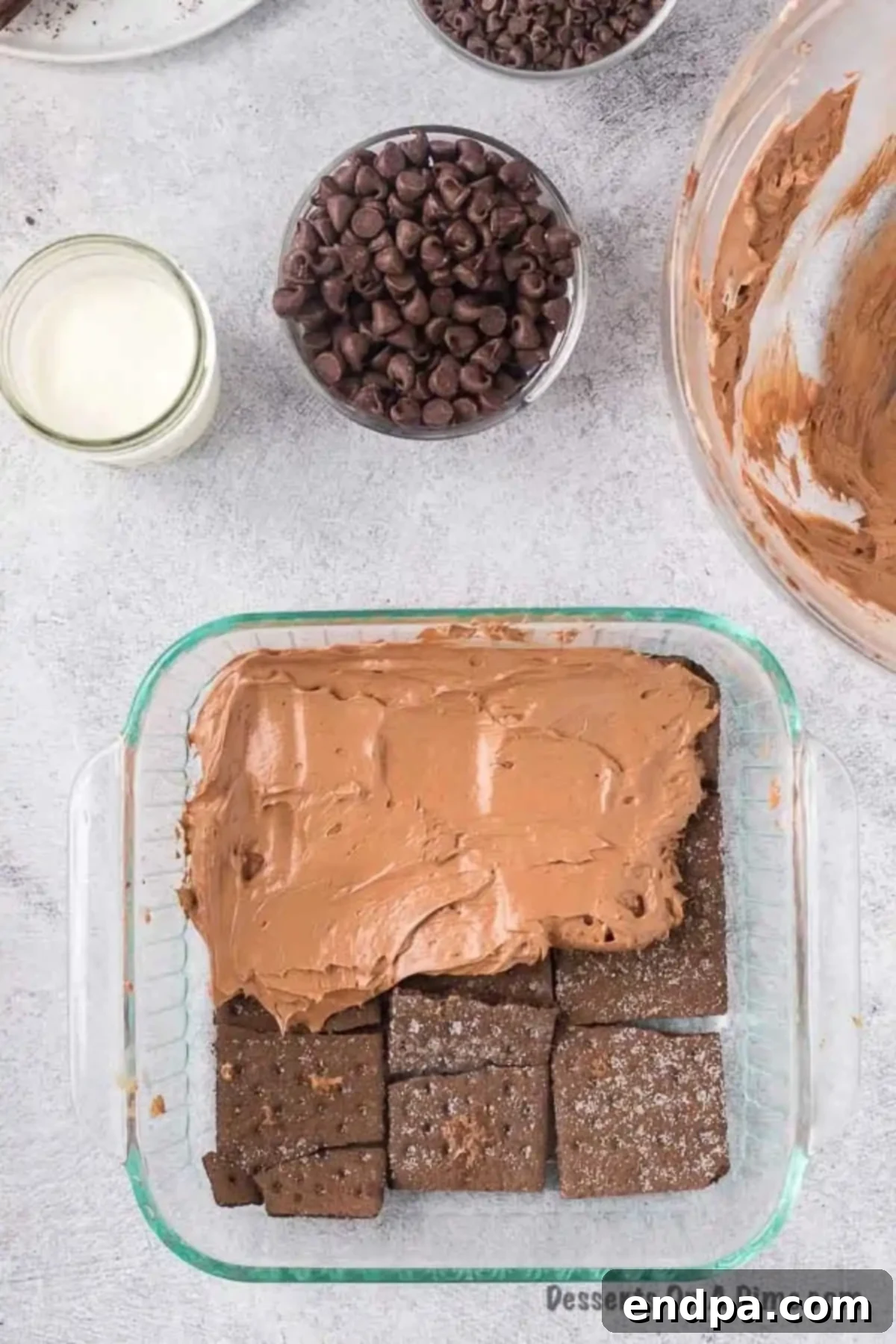 Chocolate cream cheese mixture being spread evenly over a layer of graham crackers in a baking dish.