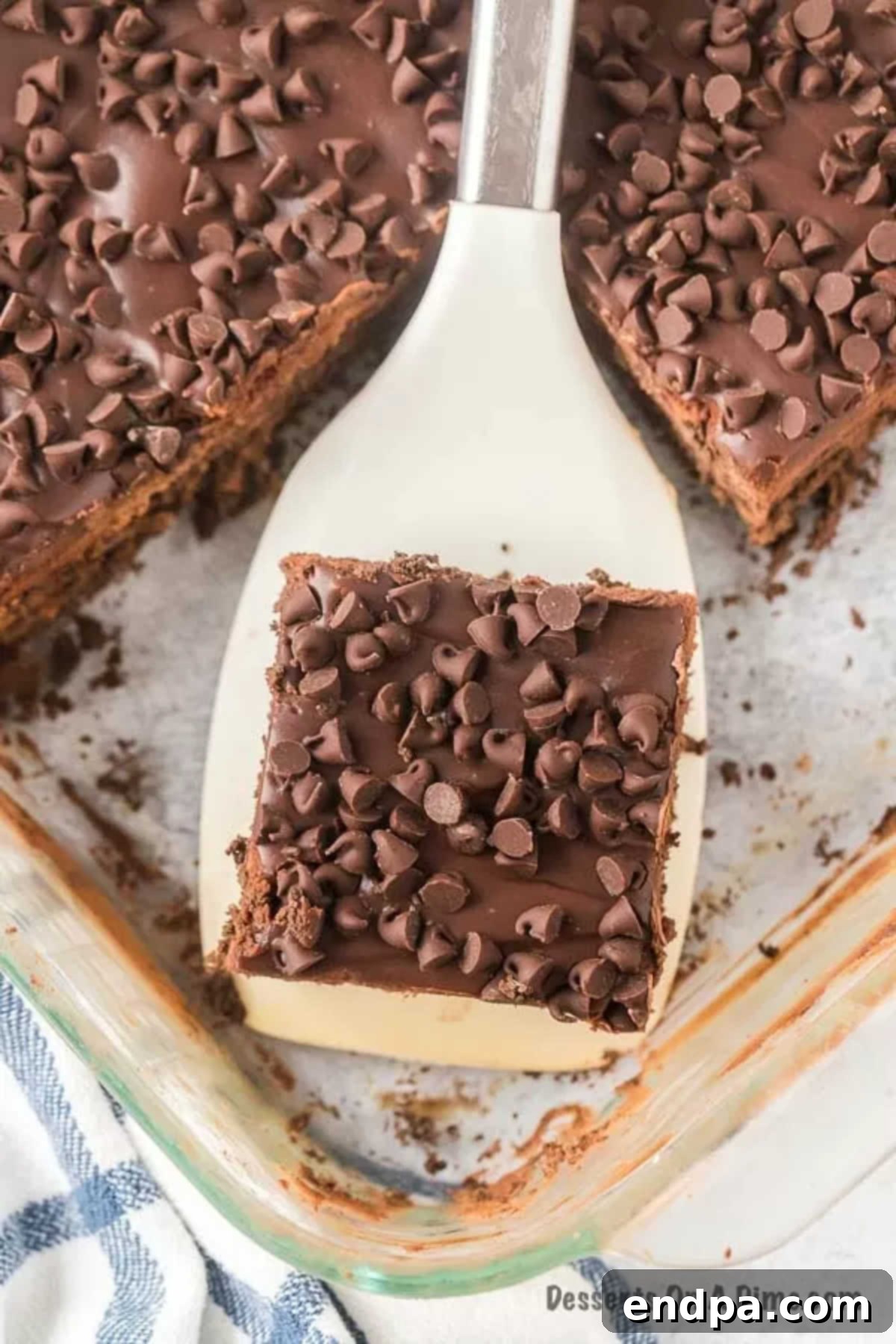 A hand serving a slice of chocolate icebox cake from the pan, showing the distinct layers.