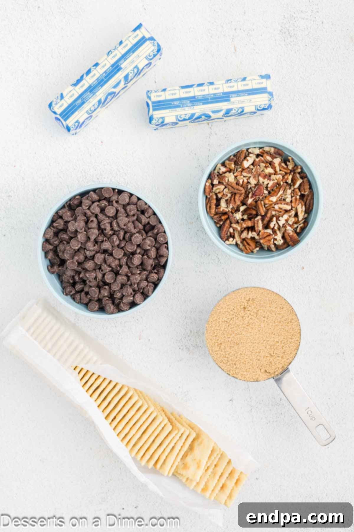 Sweet and Salty Toffee Bark 3 Ingredients for Saltine Toffee laid out: saltine crackers, sticks of butter, brown sugar, a bowl of chocolate chips, and chopped pecans.