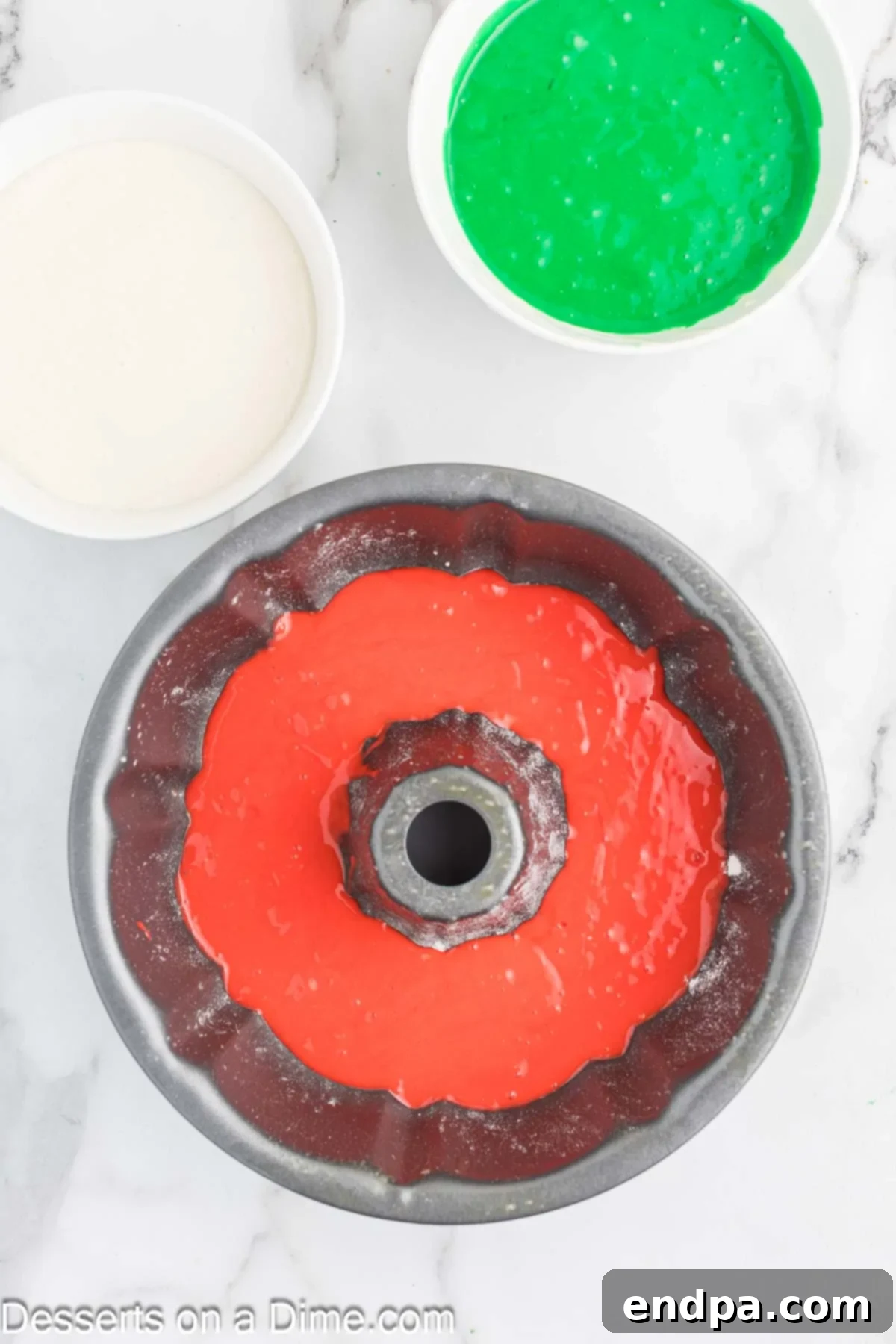 Red cake batter dolloped on top of the white batter in the Bundt pan.