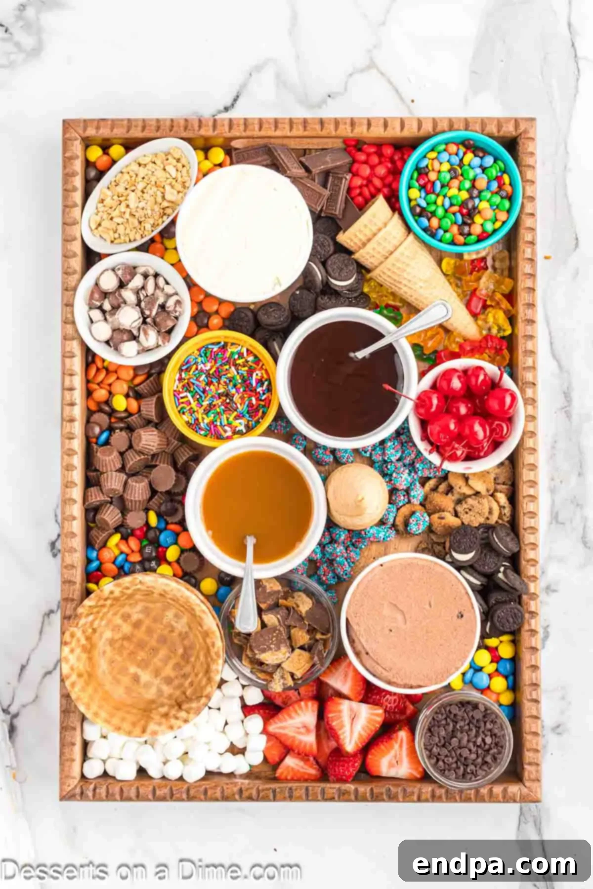 An ice cream charcuterie board with all toppings, including sauces, fruits, and candies, meticulously arranged around the ice cream pints.