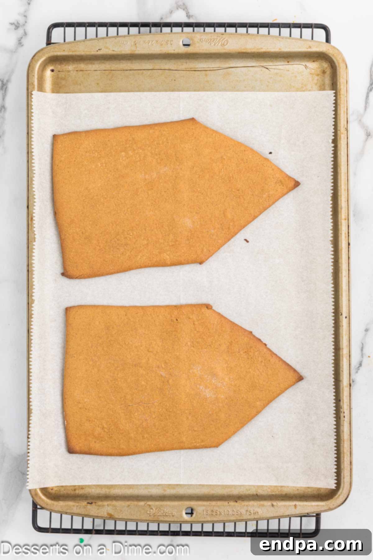 Spiced Sugar Sanctuary 9 Baked gingerbread house pieces cooling on the baking sheet after being removed from the oven, with slightly browned edges.