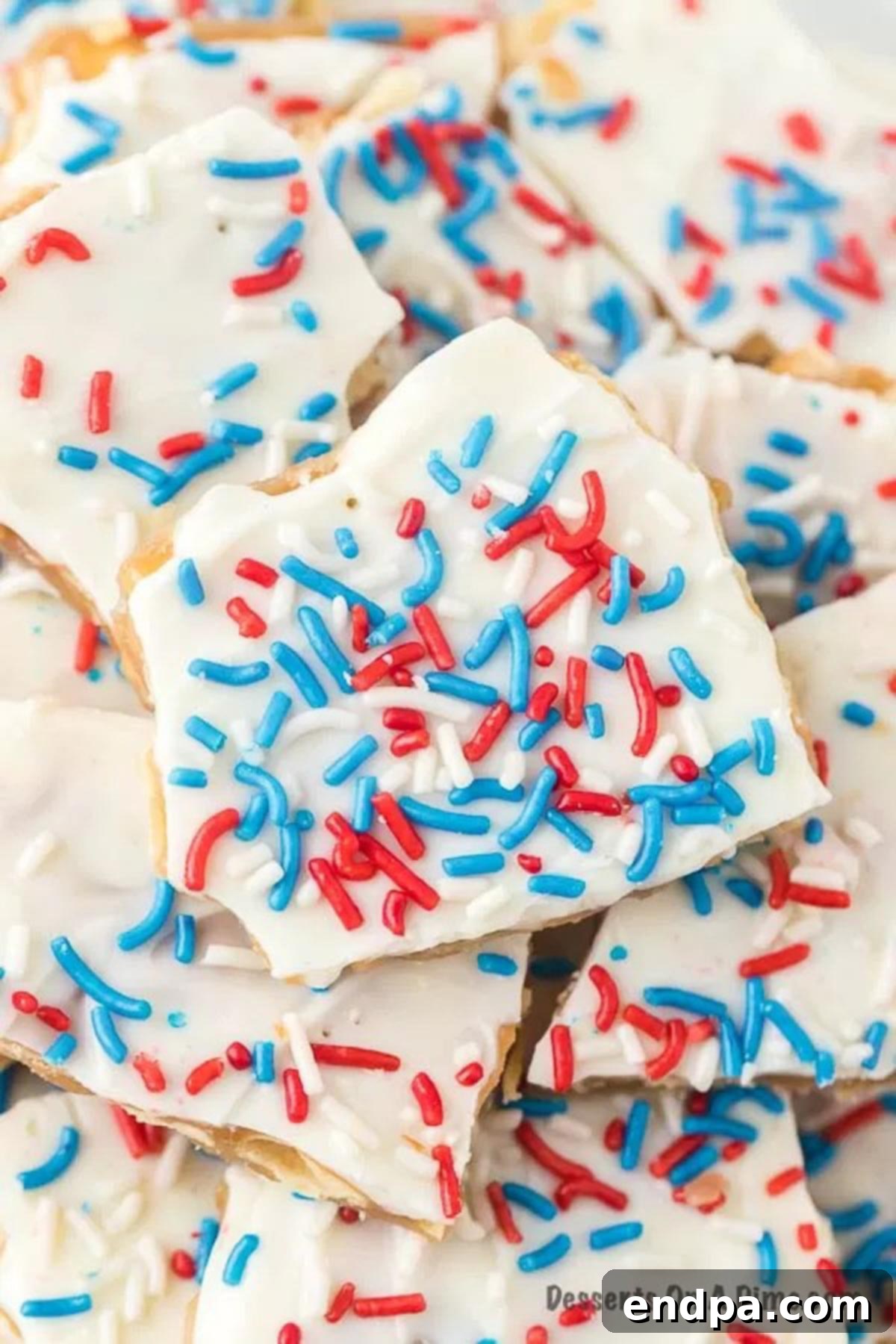 A close-up view of beautifully stacked Patriotic Cracker Toffee pieces, glistening with white chocolate and vibrant red, white, and blue sprinkles, ready for a festive celebration.