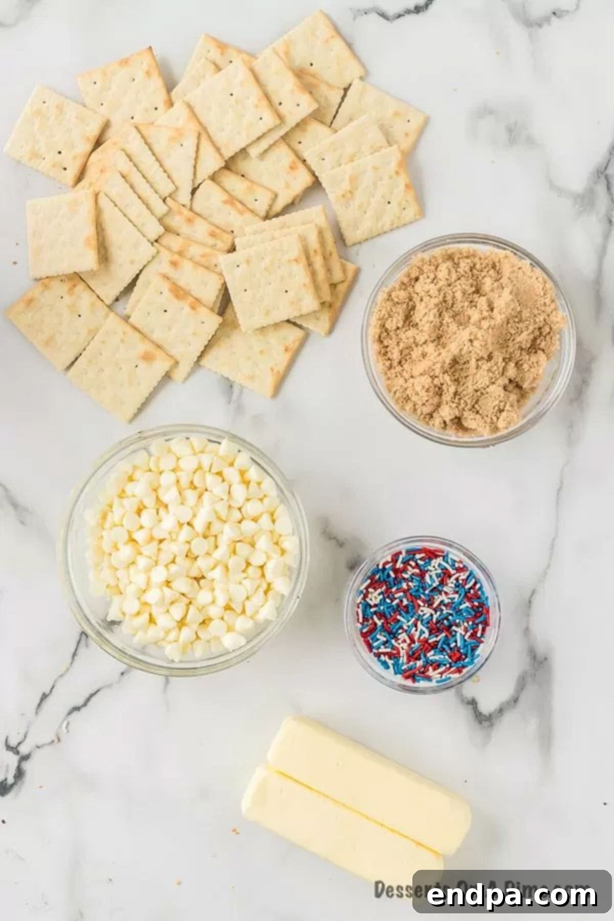 A visual display of the key ingredients for Patriotic Cracker Toffee: creamy butter sticks, rich brown sugar, glistening white chocolate chips, and a colorful mix of red, white, and blue sprinkles, laid out for preparation.
