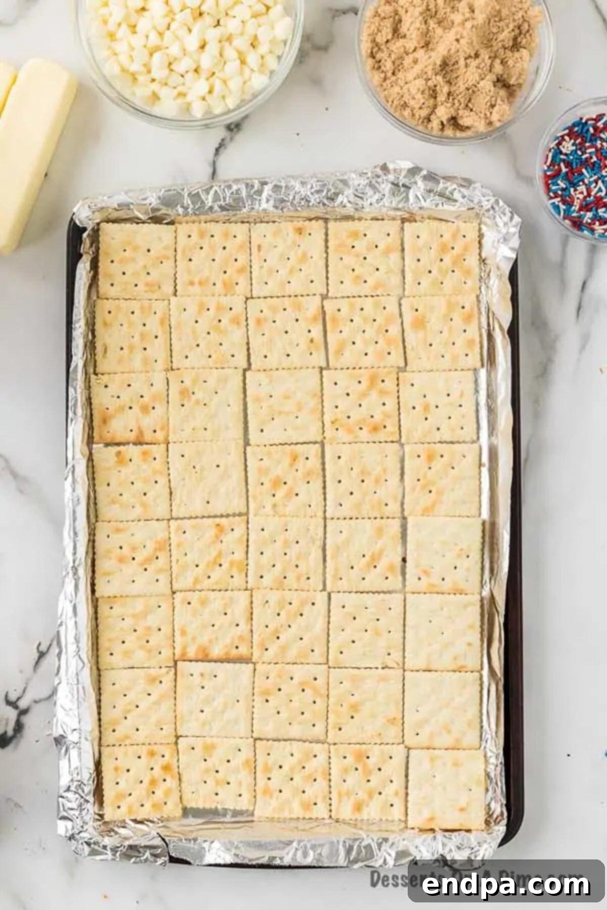 Saltine crackers meticulously arranged in a single layer on a foil-lined baking sheet, forming the crisp base for the Patriotic Cracker Toffee.