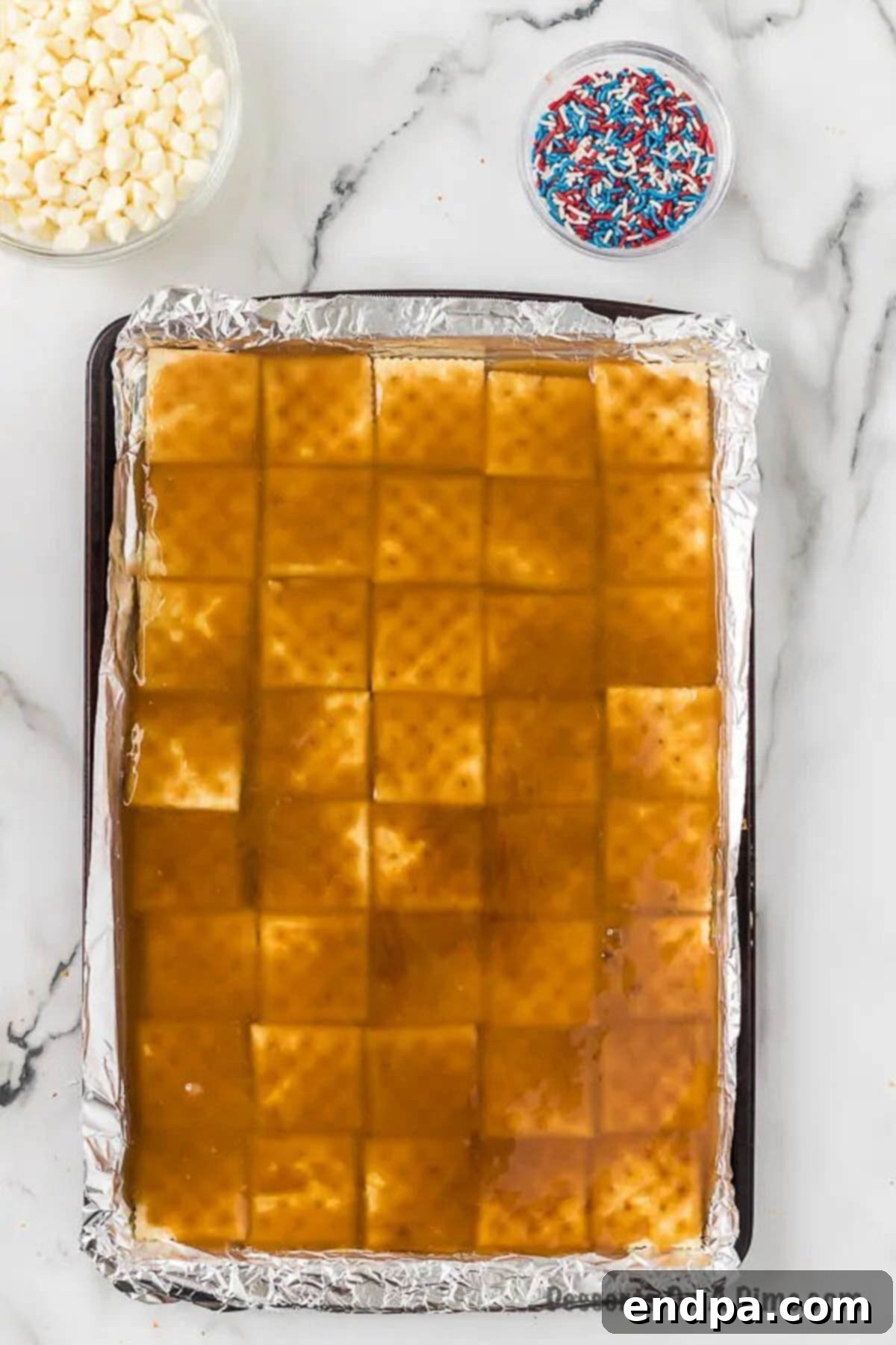 The golden brown sugar and butter toffee mixture expertly poured and spread over the crisp saltine crackers on a baking sheet, ready for the oven to caramelize further.