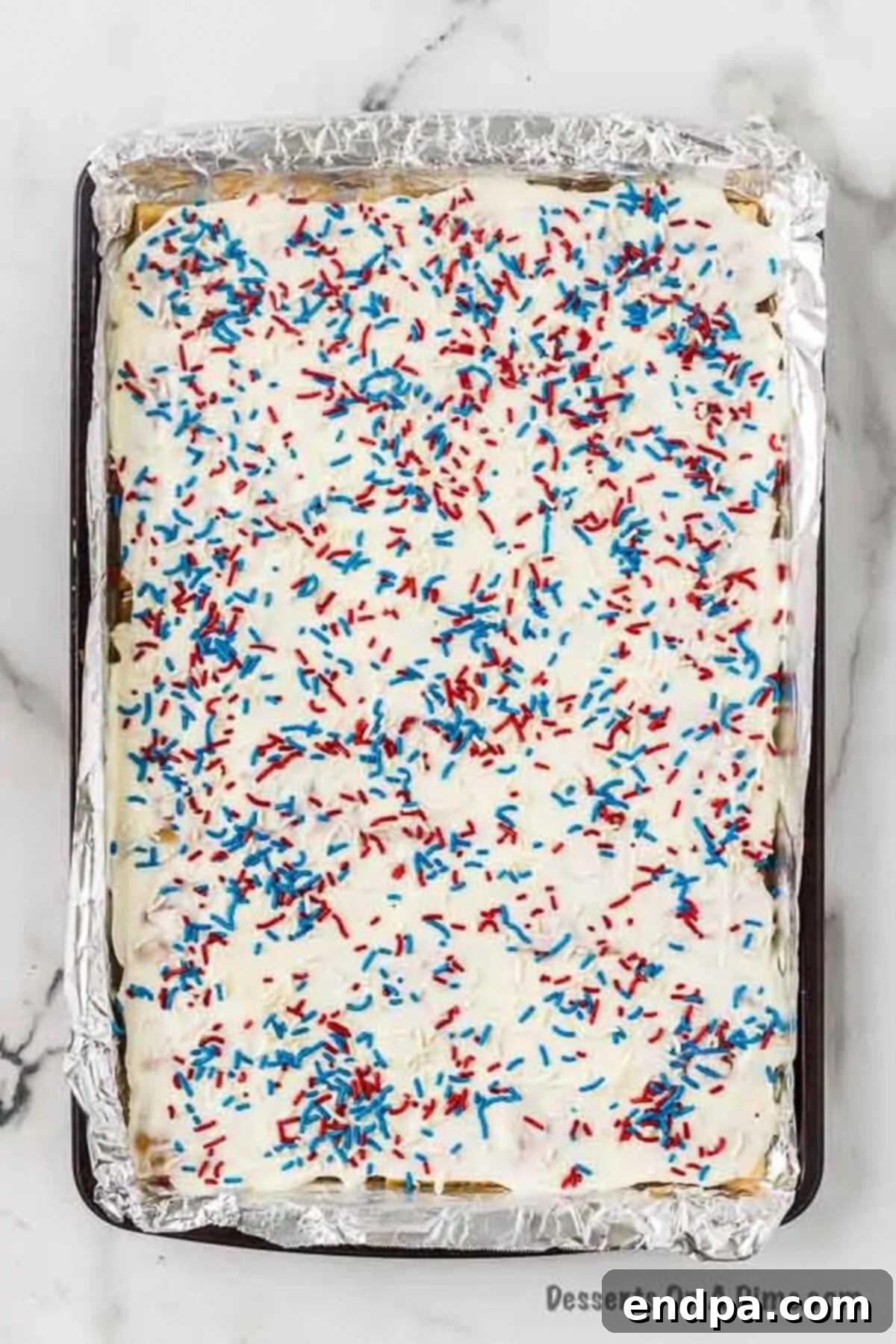 A vibrant scattering of red, white, and blue patriotic sprinkles adorning the still-warm, melted white chocolate layer, creating a festive and visually appealing finish for the cracker toffee.