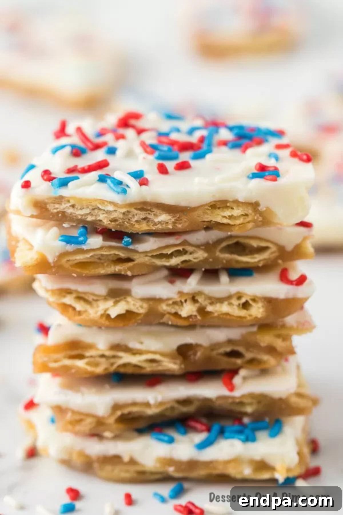 Irregularly broken pieces of Patriotic Cracker Toffee stacked artfully, showcasing distinct layers of crunchy cracker, golden toffee, creamy white chocolate, and vibrant colorful sprinkles, ready for serving.