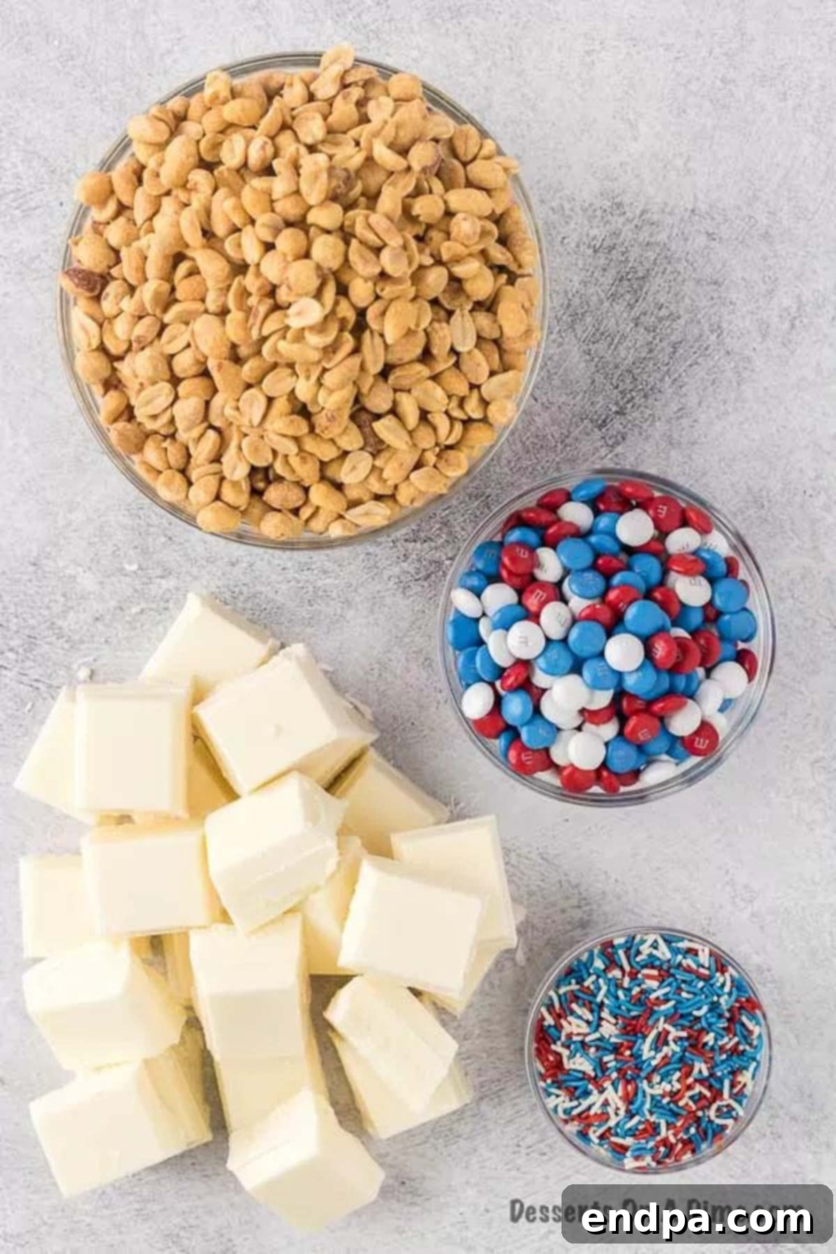 Ingredients needed to make crock pot Patriotic Clusters: peanuts, white almond bark, M&M's, and sprinkles, laid out on a clean surface.