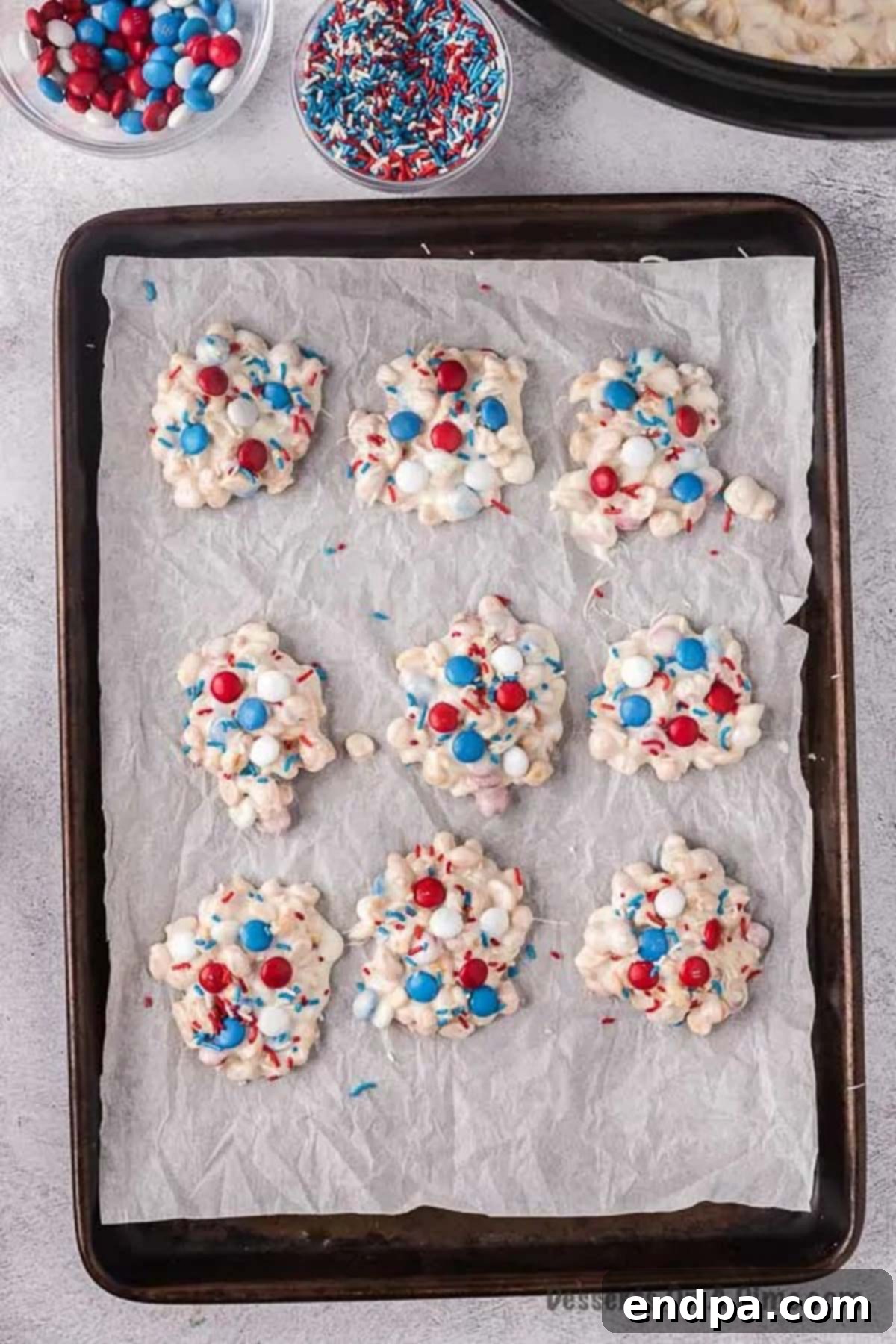 Finished candy clusters arranged on a baking sheet lined with wax paper, decorated with sprinkles and M&M's.