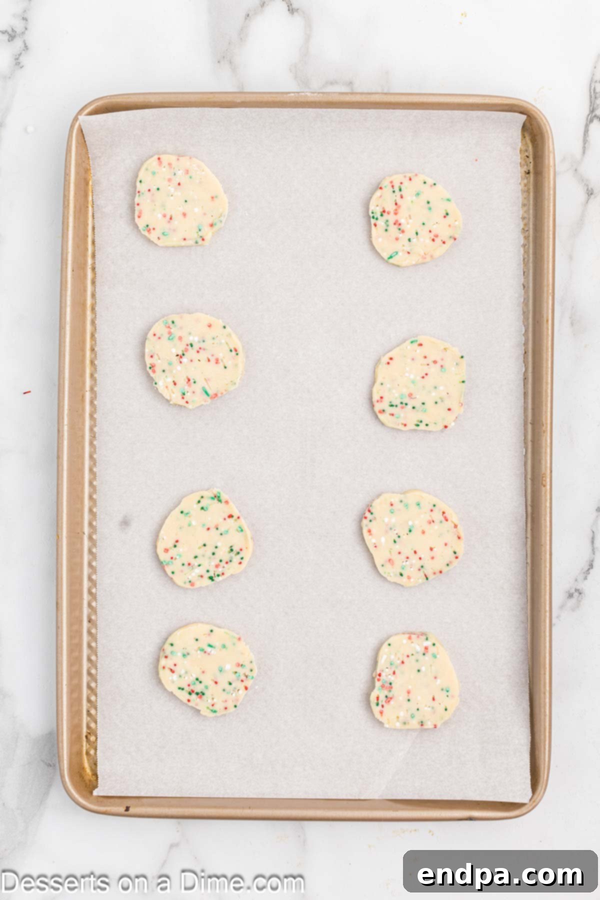 Buttery Christmas Shortbread Delights 8 Uniformly sliced shortbread cookie dough rounds placed onto a baking sheet.