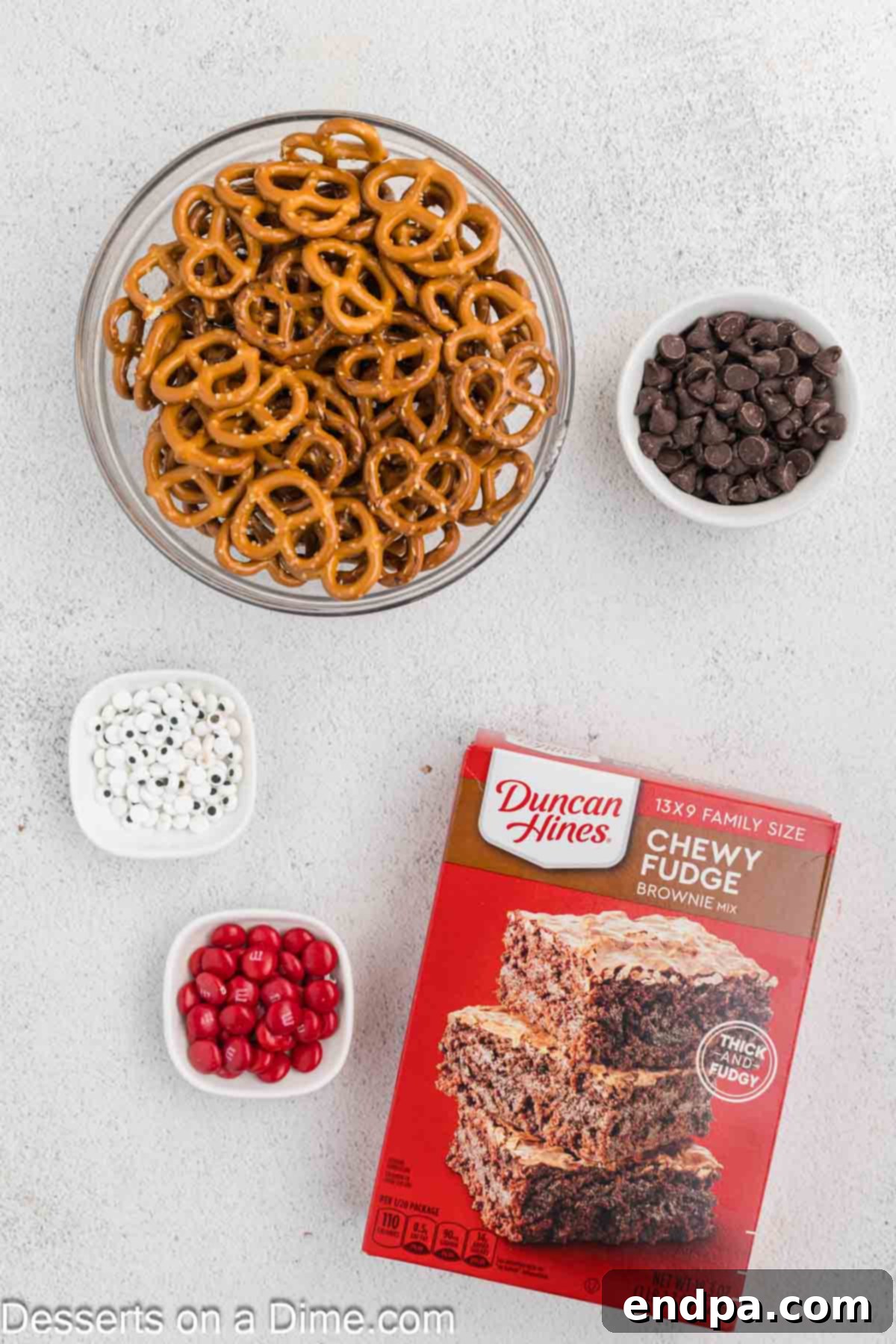 Christmas Antler Brownies 3 All ingredients for Reindeer Brownies laid out: a box brownie mix, eggs, oil, water for the brownie preparation, chocolate chips for melting, mini pretzels for antlers, candy eyes, and red M&Ms for Rudolph's nose.