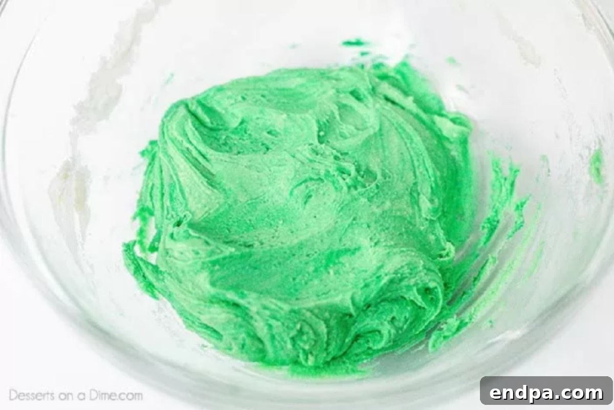 Green food coloring being mixed into a bowl of cookie dough, transforming its color to a vibrant green.