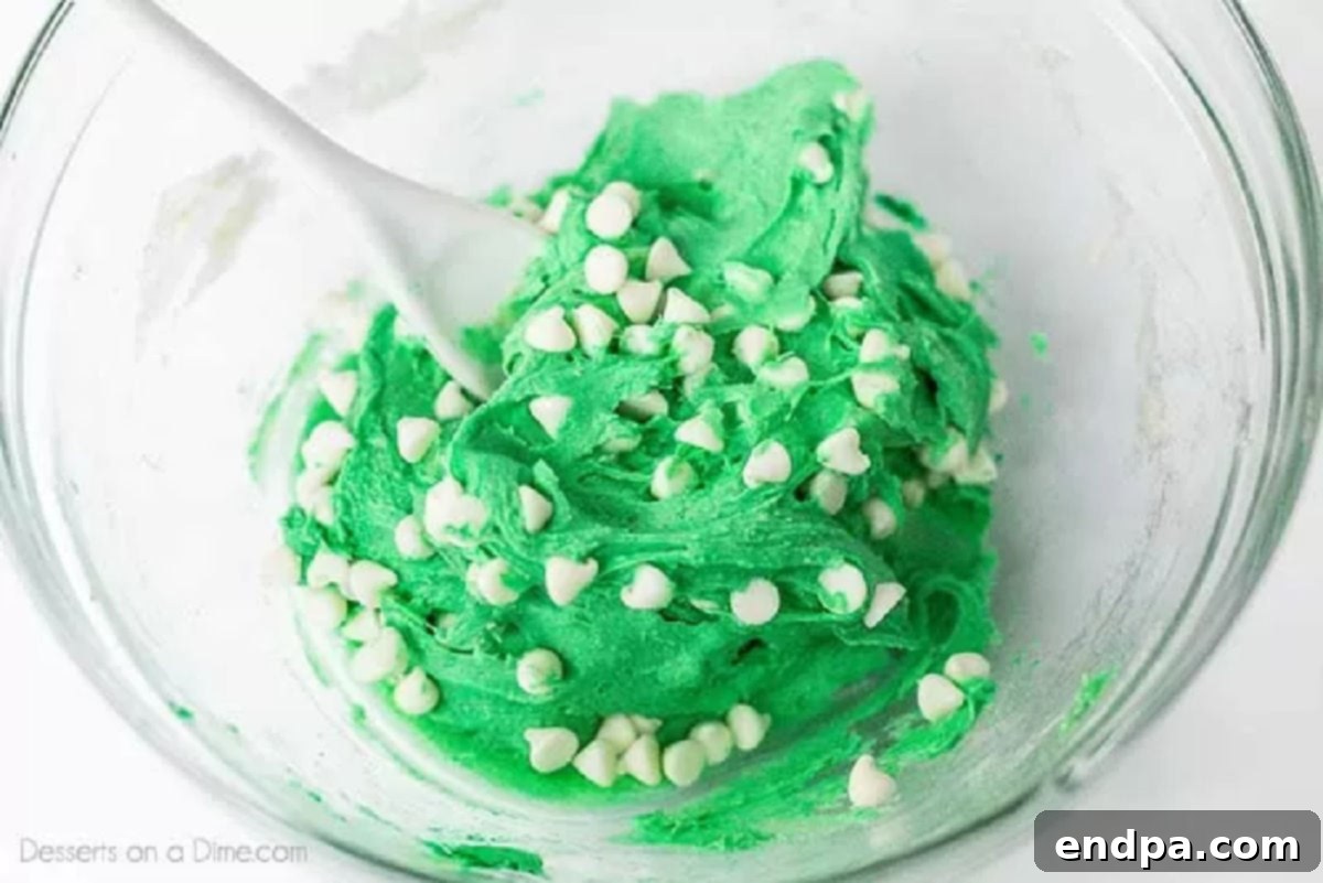 White chocolate chips carefully folded into the green cookie dough in a mixing bowl.