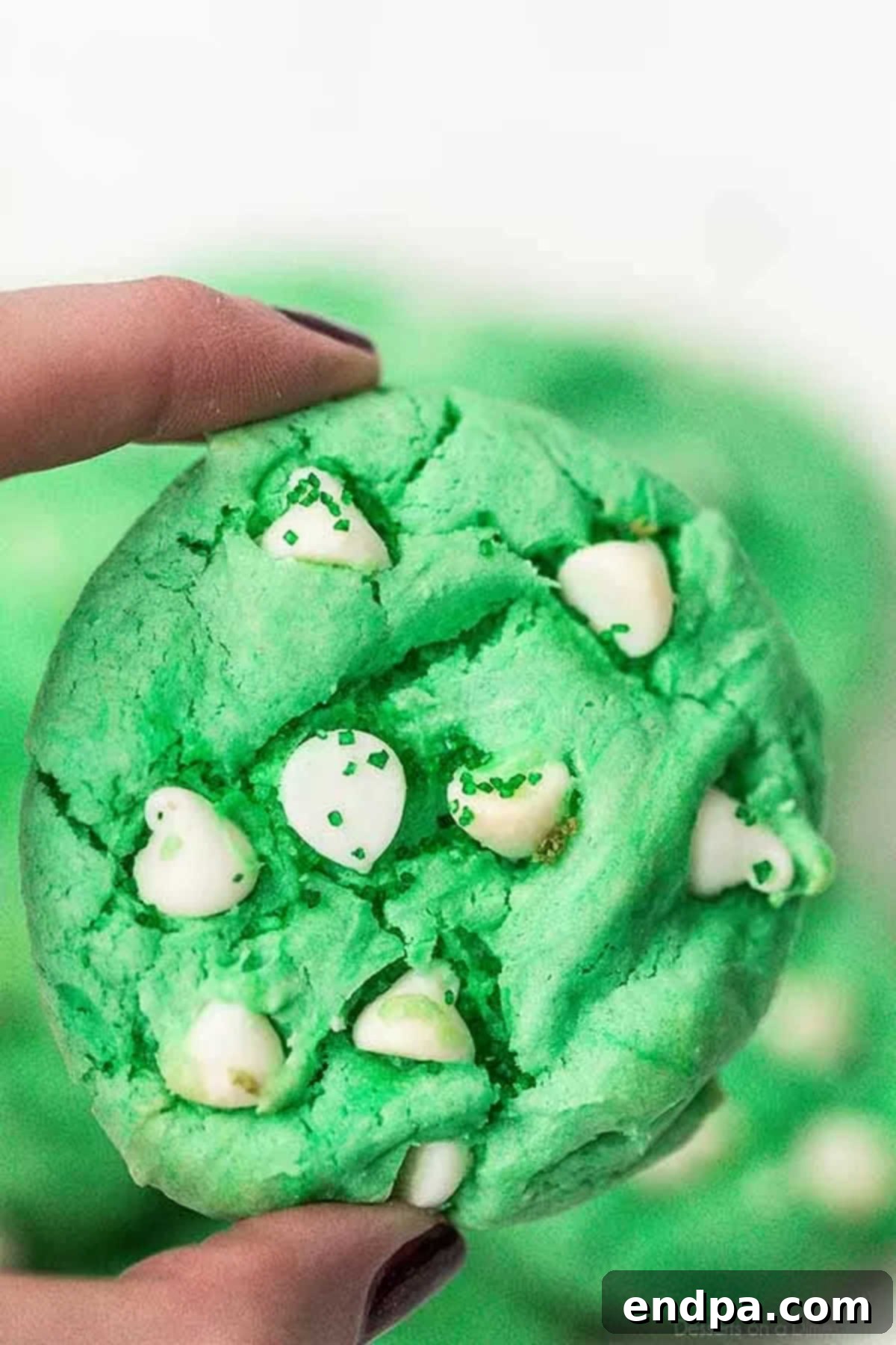 A hand holding up a vibrant green St. Patrick's Day cookie with visible white chocolate chips, showcasing its festive color and delicious texture.