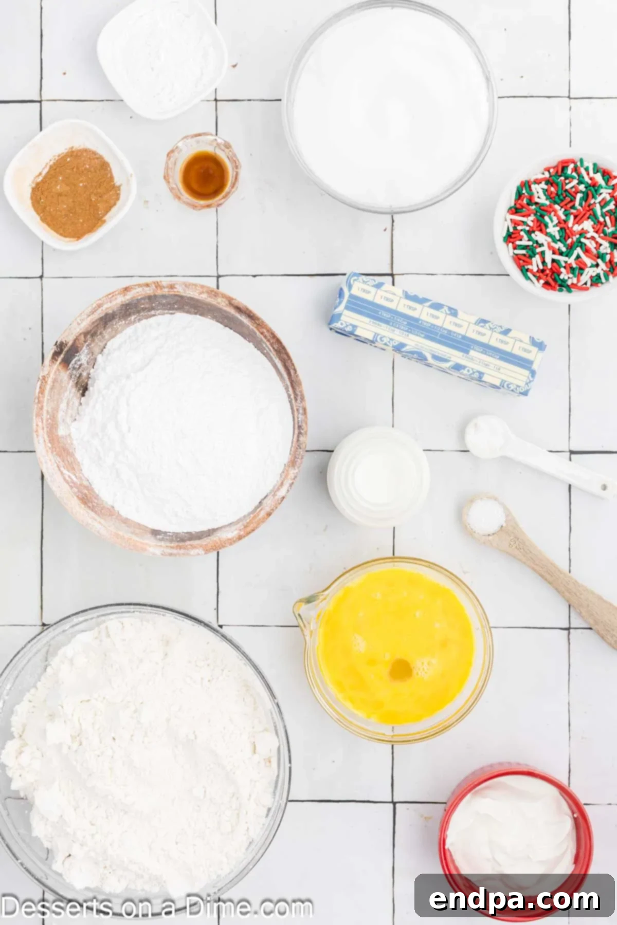Yuletide Bake 3 Ingredients for Christmas Bread arranged on a surface, including flour, baking soda, cinnamon, butter, eggs, sour cream, whole milk, Christmas sprinkles, and vanilla extract.