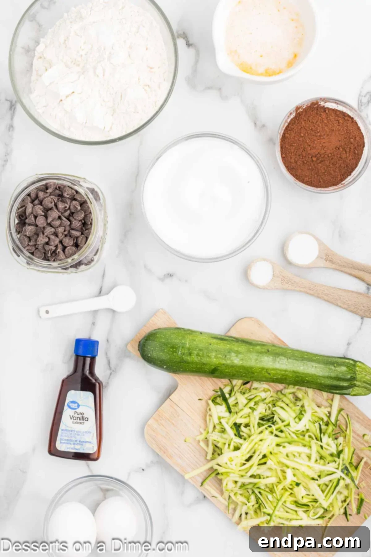 Fudgy Chocolate Zucchini Bread 3 A display of ingredients for chocolate zucchini bread: flour, cocoa powder, baking soda, eggs, vanilla extract, shredded zucchini, and chocolate chips.
