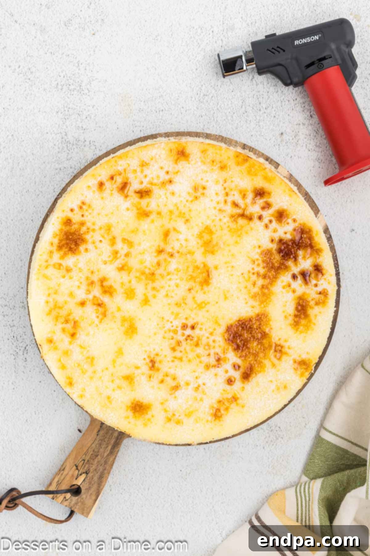 Crispy Caramel Cheesecake 12 A kitchen torch being used to caramelize the sugar topping on the cheesecake, creating a golden, glassy brûlée crust.