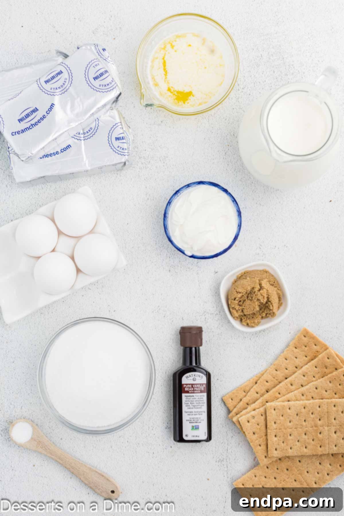 Crispy Caramel Cheesecake 3 Ingredients for Cheesecake Brulee arranged on a surface, including graham cracker sheets, butter, brown sugar, cream cheese blocks, vanilla bean pods, eggs, heavy cream, sour cream, and granulated sugar.