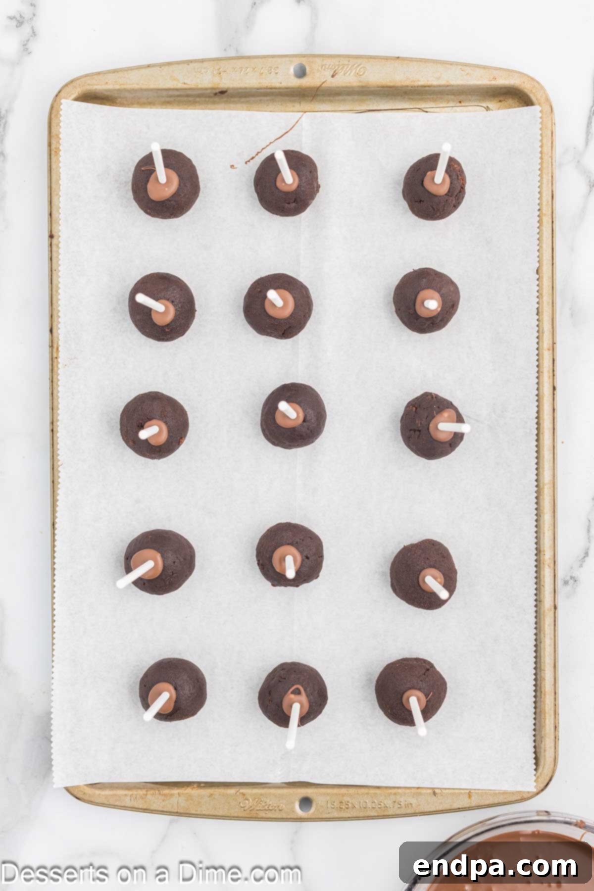 Bite Sized Chocolate Bliss 11 Chocolate cake pops with lollipop sticks inserted, sitting on a baking sheet, ready for chilling.