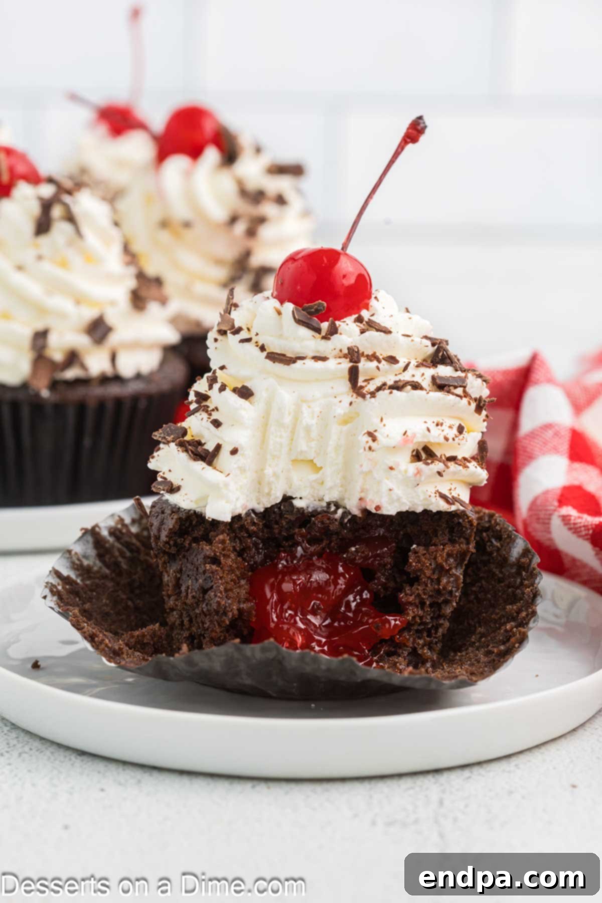 A Black Forest cupcake cut in half, revealing the chocolate cake, cherry compote filling, and whipped cream topping.