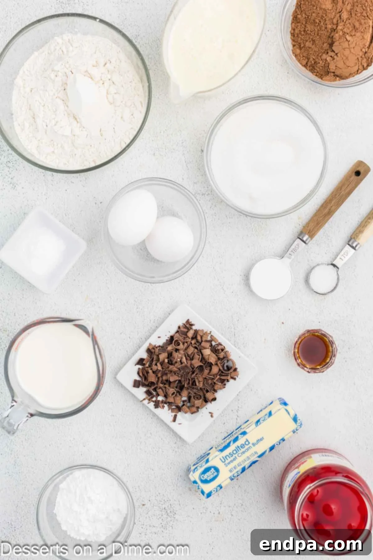 Ingredients laid out for Black Forest Cupcakes: flour, cocoa powder, baking soda, butter, eggs, buttermilk, vanilla, maraschino cherries, cornstarch, heavy whipping cream, powdered sugar, and chocolate shavings.