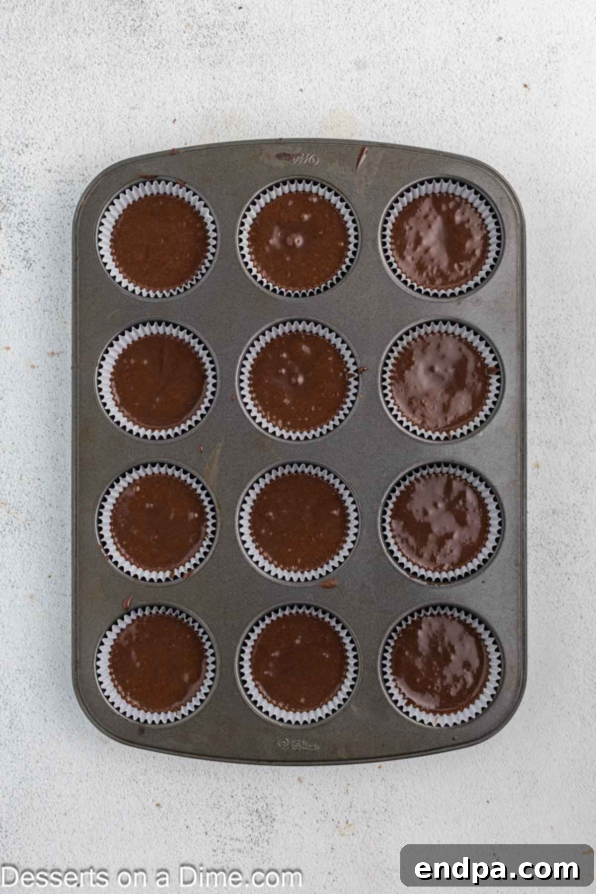 Cupcake batter being poured into cupcake liners in a muffin pan.