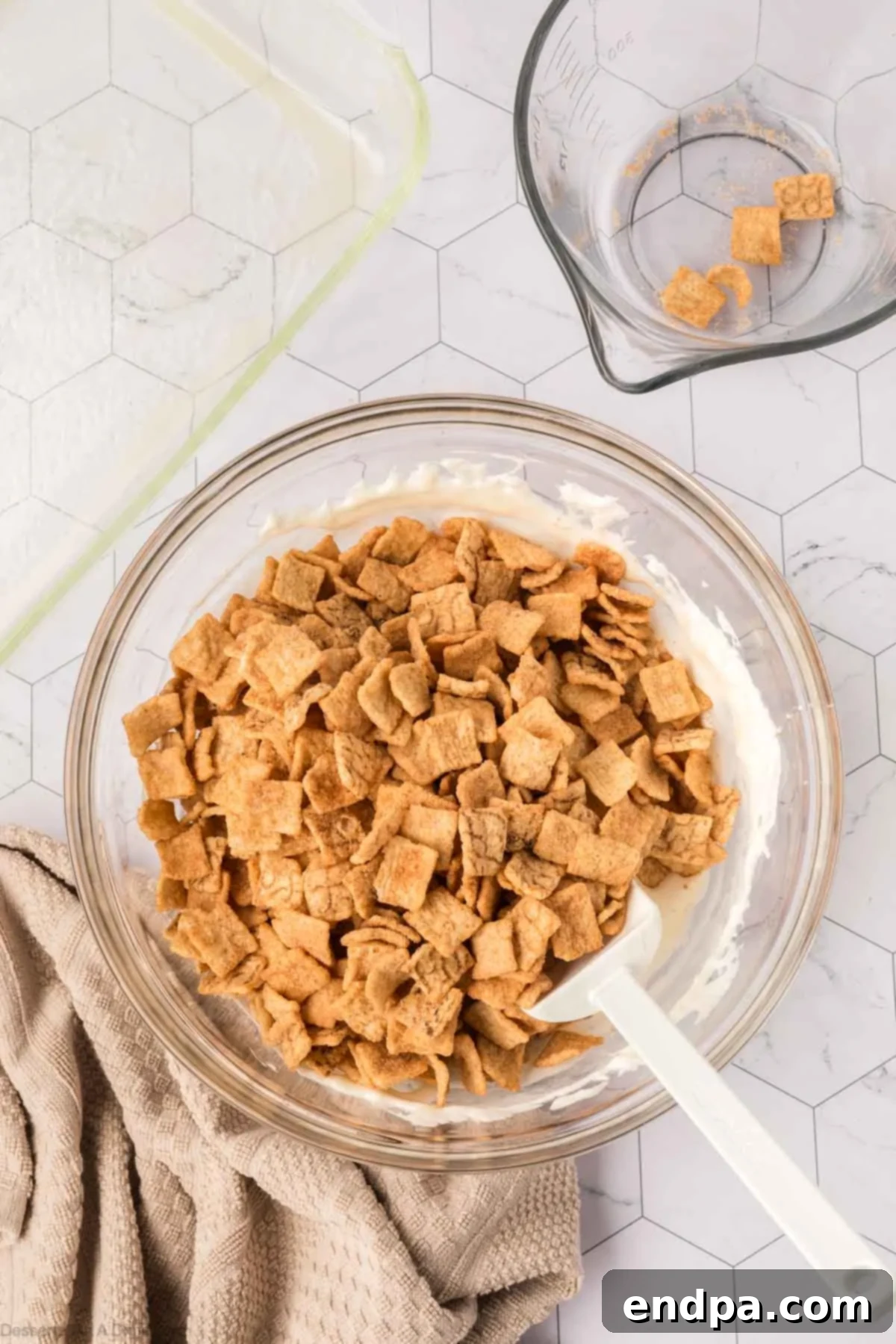 Cinnamon Toast Crunch cereal being gently folded into the warm, melted marshmallow mixture.