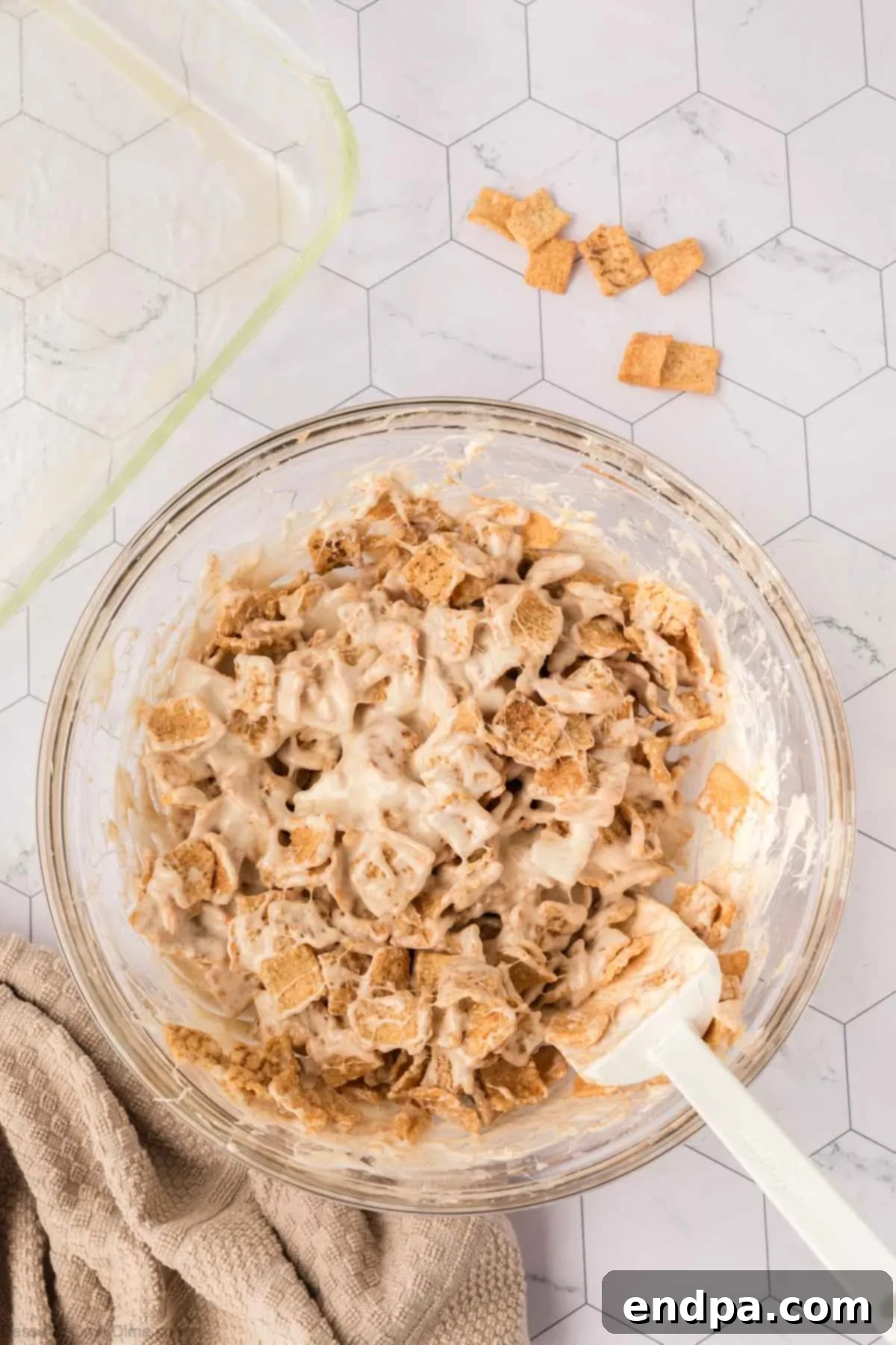 Cereal fully combined with the marshmallow mixture in a bowl, ready to be pressed into the prepared pan.