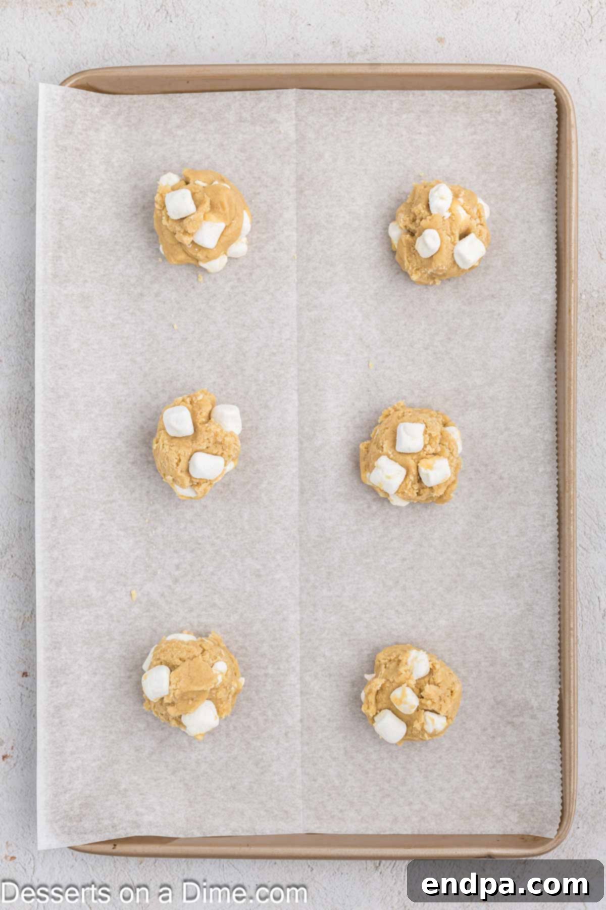 Fluffy Cloud Cookies 8 Cookie dough balls are scooped onto a baking sheet and topped with additional mini marshmallows before baking.