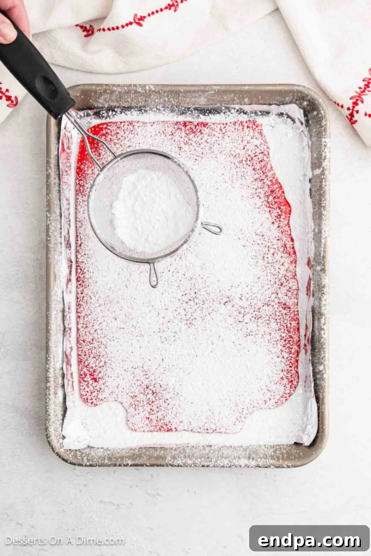 Remaining powdered sugar being sprinkled evenly over the still-warm, poured hard candy mixture.