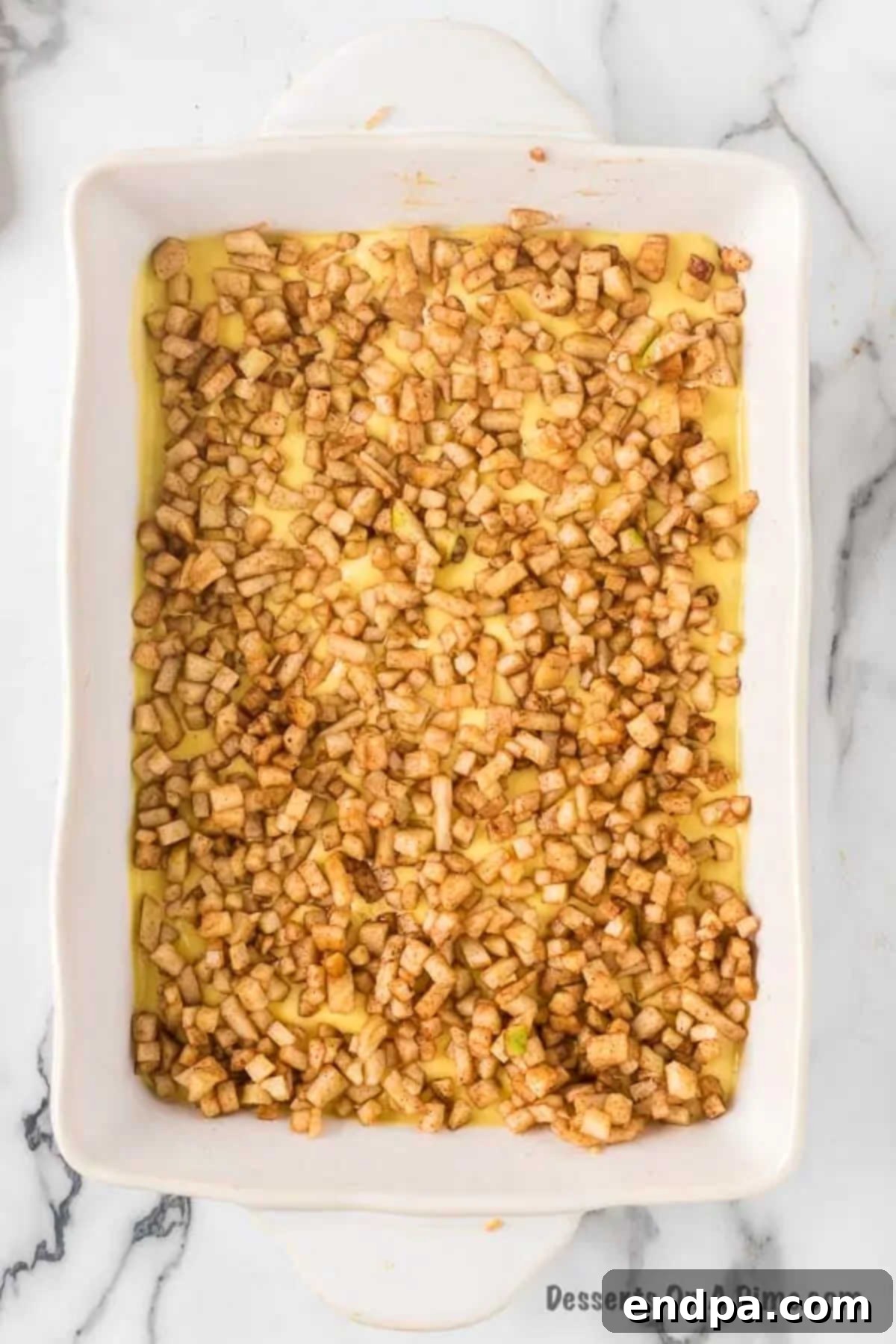 The spiced apple mixture evenly spooned and spread over the creamy cheesecake layer in the baking dish.
