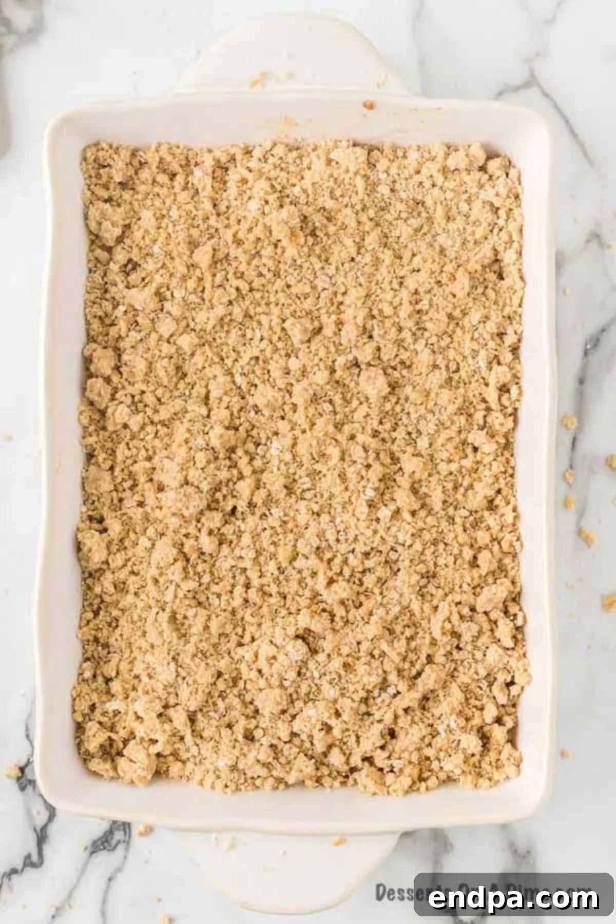 The crumbly streusel topping evenly sprinkled over the spiced apple layer in the baking dish, ready for baking.