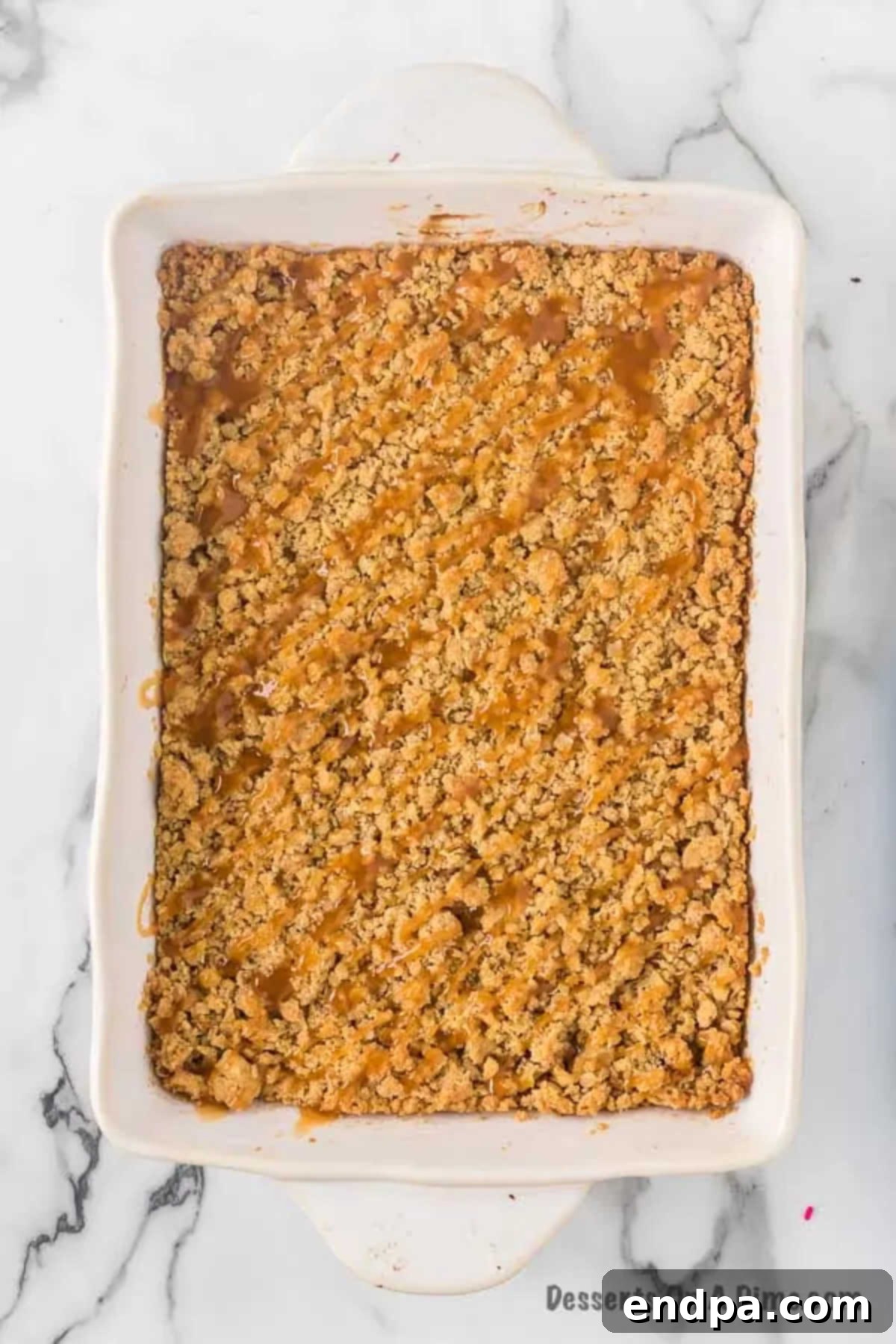 Freshly baked Caramel Apple Cheesecake Bars, golden brown and glistening with a generous drizzle of caramel sauce over the top.