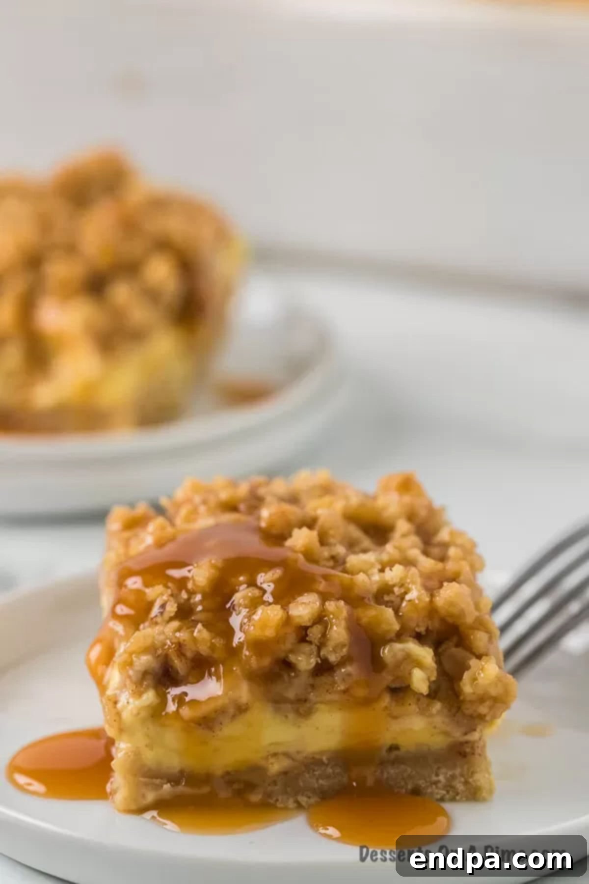 Close-up overhead shot of a single Caramel Apple Cheesecake bar on a white plate, showing the texture of the streusel and the caramel drizzle.