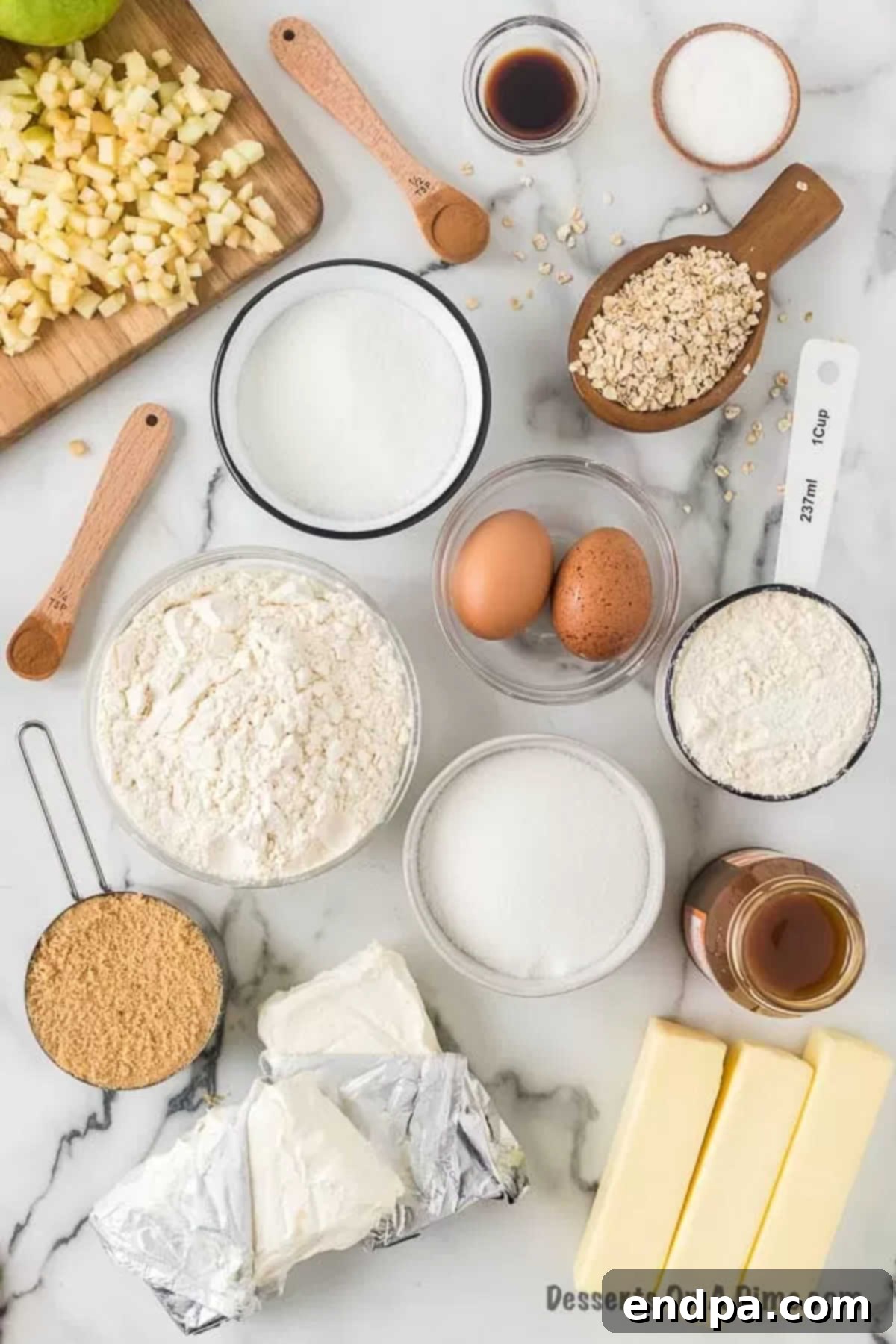 A vibrant flat lay showing all the fresh ingredients needed for Caramel Apple Cheesecake Bars, including bags of flour and brown sugar, a stick of softened butter, a block of cream cheese, fresh eggs, vanilla extract, bright green Granny Smith apples, and small bowls of ground cinnamon and nutmeg.
