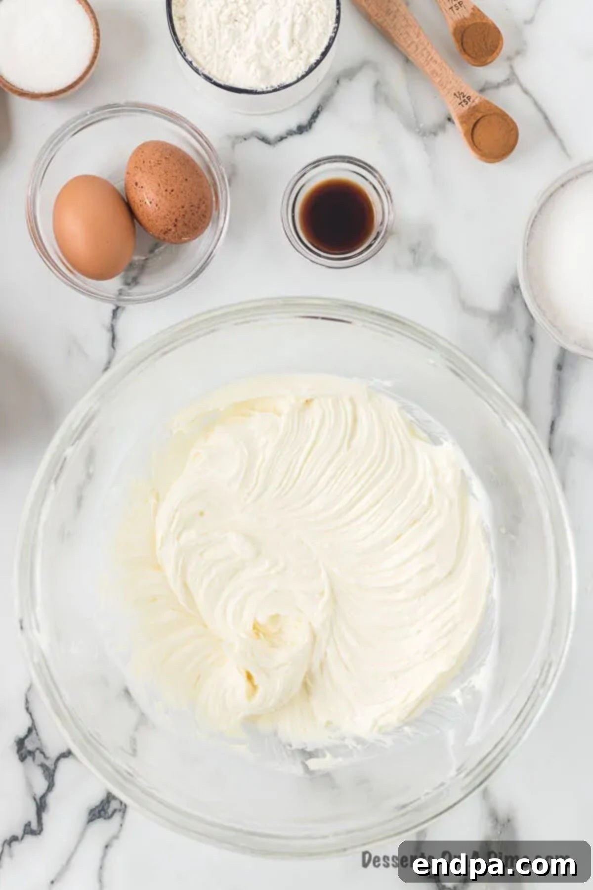 Softened cream cheese and granulated sugar being beaten together in a large mixing bowl.
